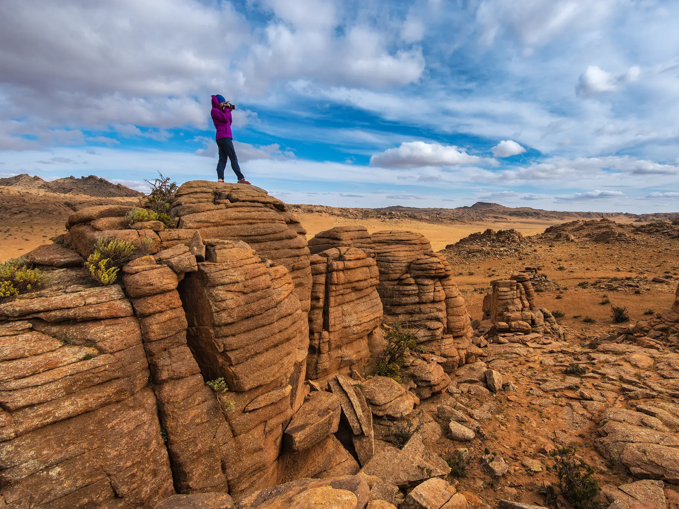 Eine Wanderin fotografiert von einer bizarren Felsformation in Baga Gazriin Chuluu die weite Landschaft der Wüste Gobi in der Mongolei.