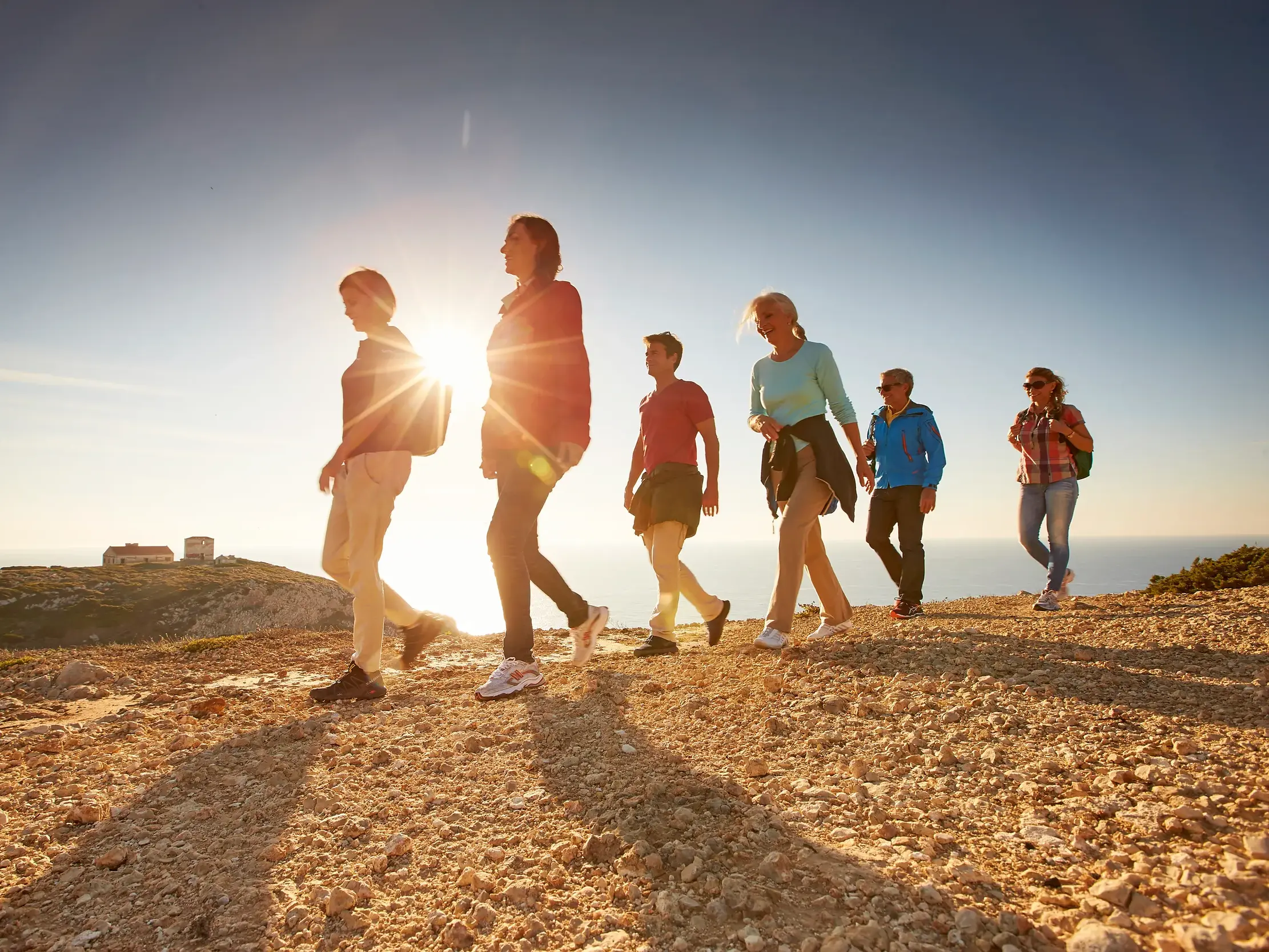 Eine Studiosus Reisegruppe wandert bei Sonnenuntergang auf einem Küstenpfad an der Steilküste der Algarve mit Blick auf den Atlantik.