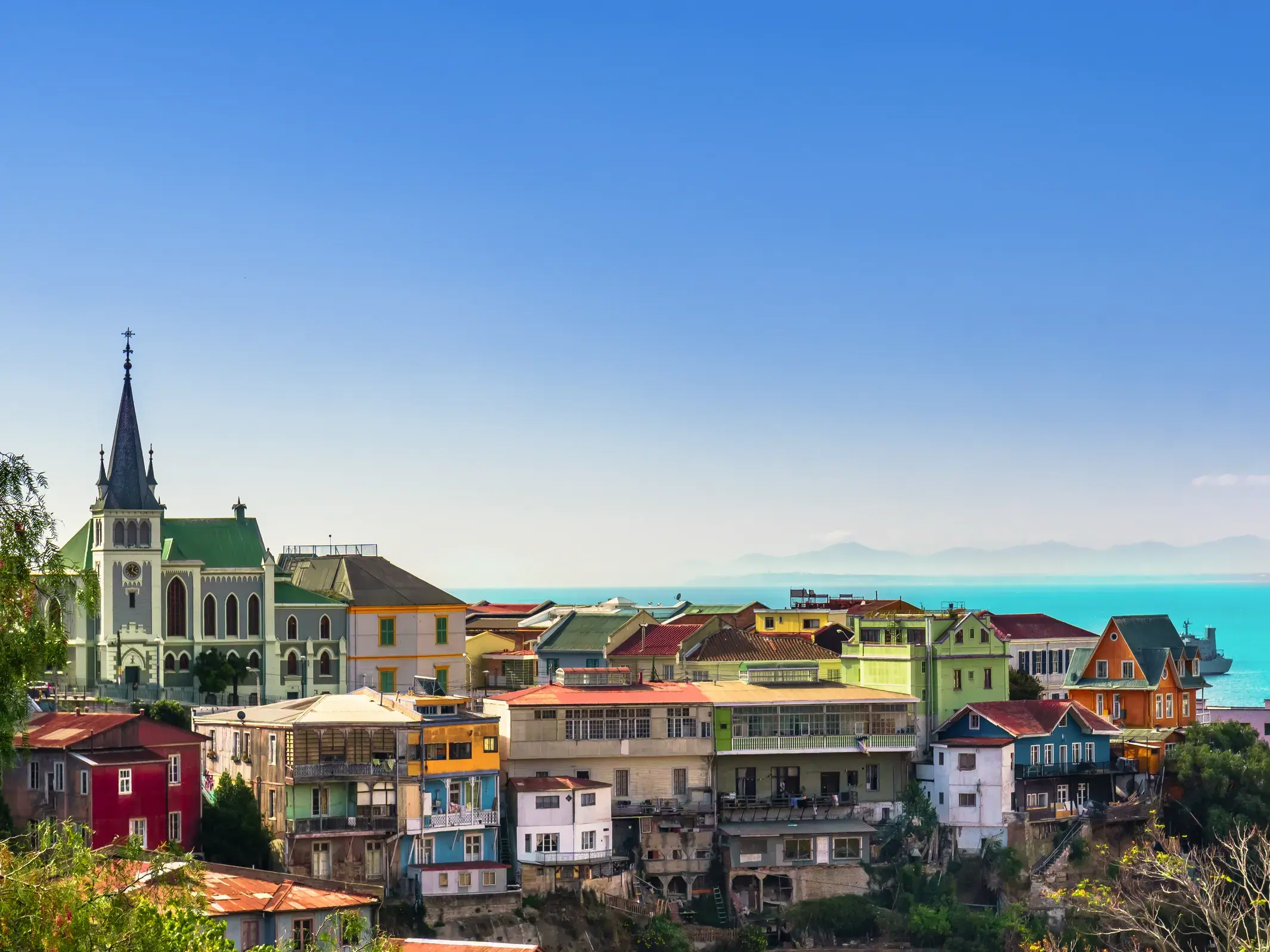 Die bunten Häuser der UNESCO-Stadt Valparaíso schmiegen sich an einen Hügel mit Blick auf das türkise Meer und die Anden.