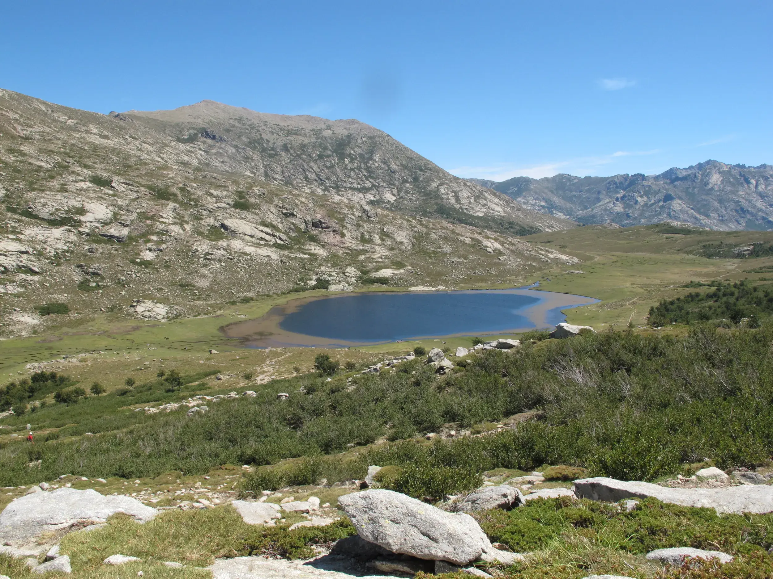 Sonniger Blick über die korsische Berglandschaft auf den tiefblauen Lac de Nino beim Trekking auf dem Fernwanderweg GR20.