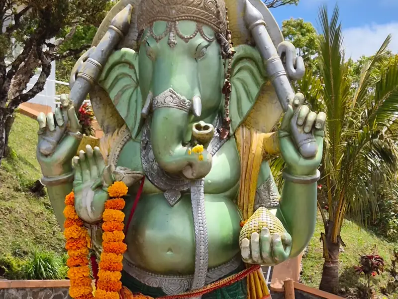 Große, grüne Statue des Hindu-Gottes Ganesha mit orangefarbener Blumengirlande am heiligen See Grand Bassin auf Mauritius.