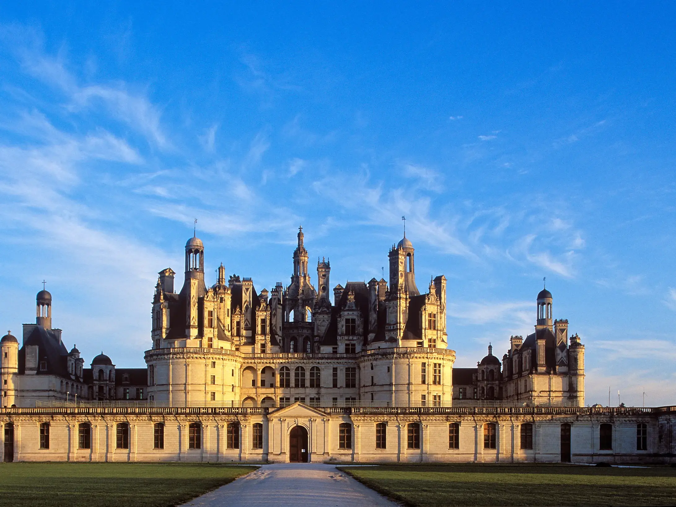 Majestätisches Schloss Chambord im Loiretal, ein Höhepunkt der Studienreise, in warmem Abendlicht unter blauem Himmel.