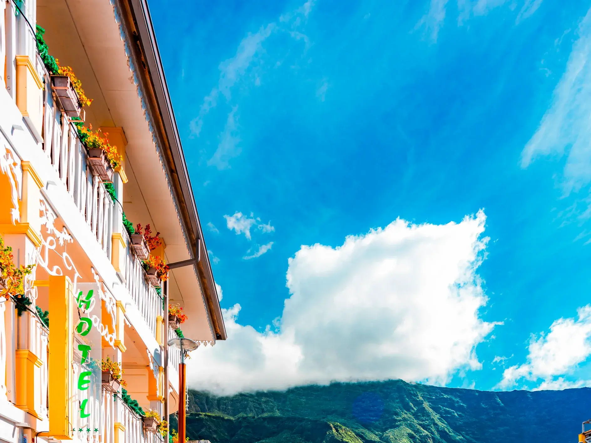 Farbenfrohe Fassade eines Hauses in Cilaos mit weißen Holzbalkonen vor einer Bergkulisse unter blauem Himmel auf La Réunion.