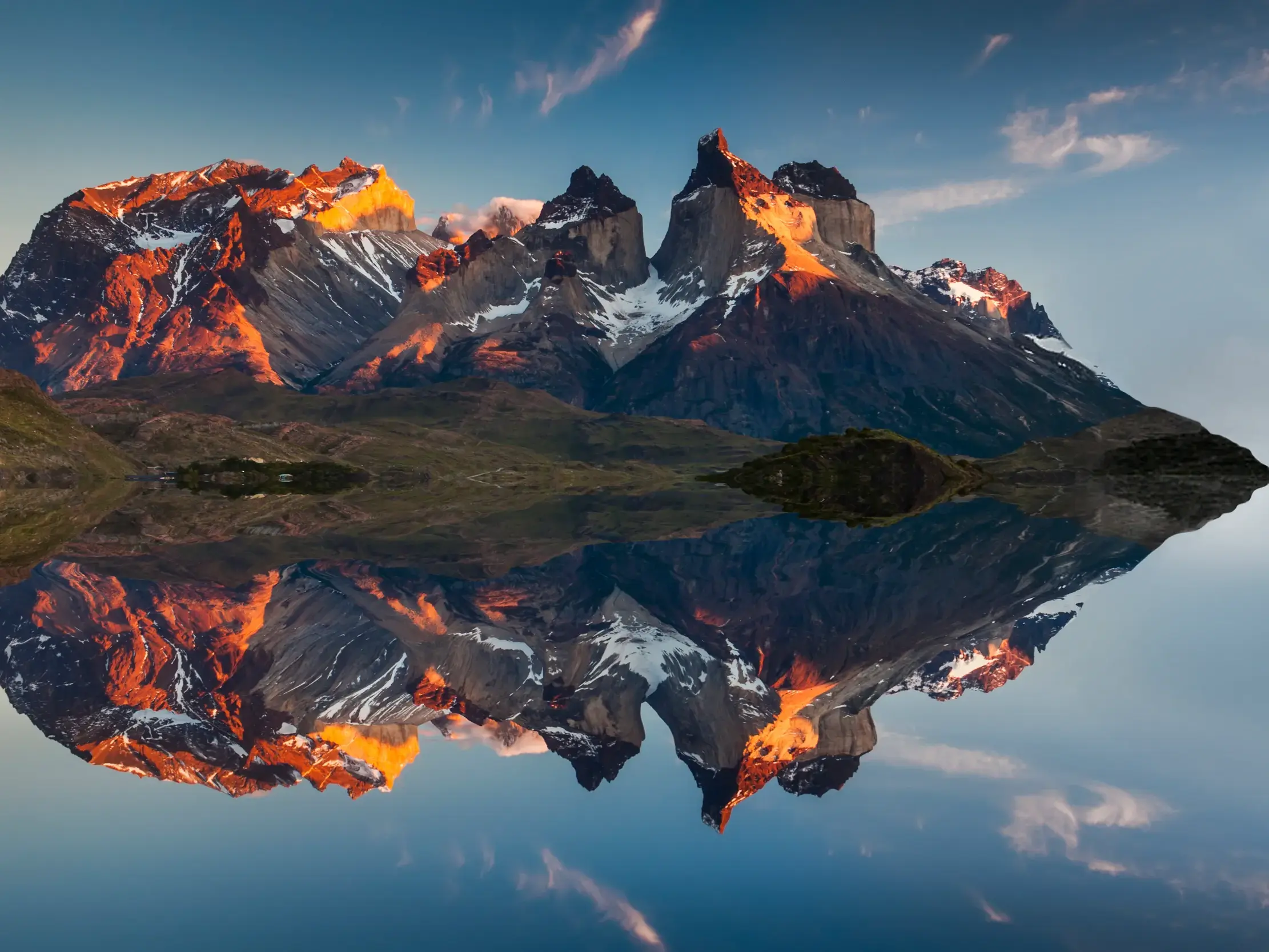 Die markanten Gipfel des Torres del Paine Nationalparks im Morgenrot, die sich makellos in einem patagonischen See spiegeln.