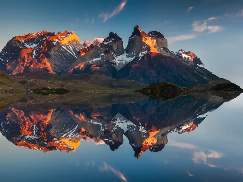 Die markanten Gipfel des Torres del Paine Nationalparks im Morgenrot, die sich makellos in einem patagonischen See spiegeln.