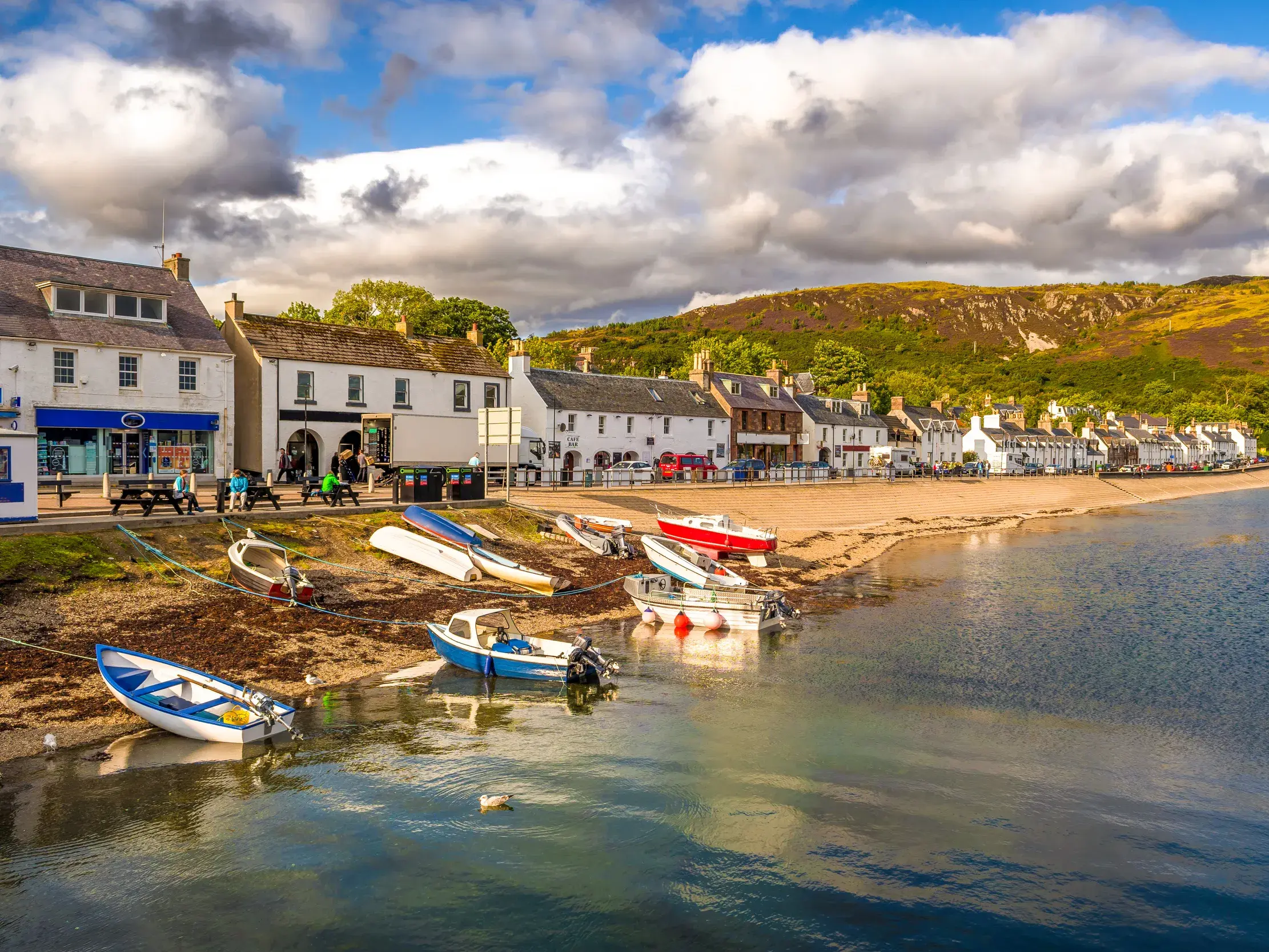 Malerische Küstenansicht des Fischerdorfs Ullapool am Loch Broom mit kleinen Booten am Ufer vor einer Häuserzeile.
