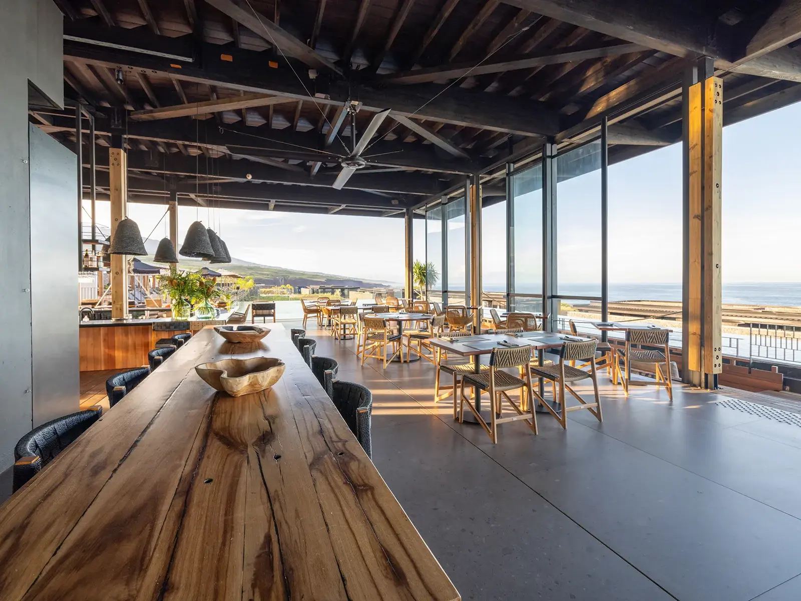 Das moderne Restaurant im Wood Hotel & Spa auf La Réunion mit langem Holztisch und Panoramablick auf das Meer im Abendlicht.
