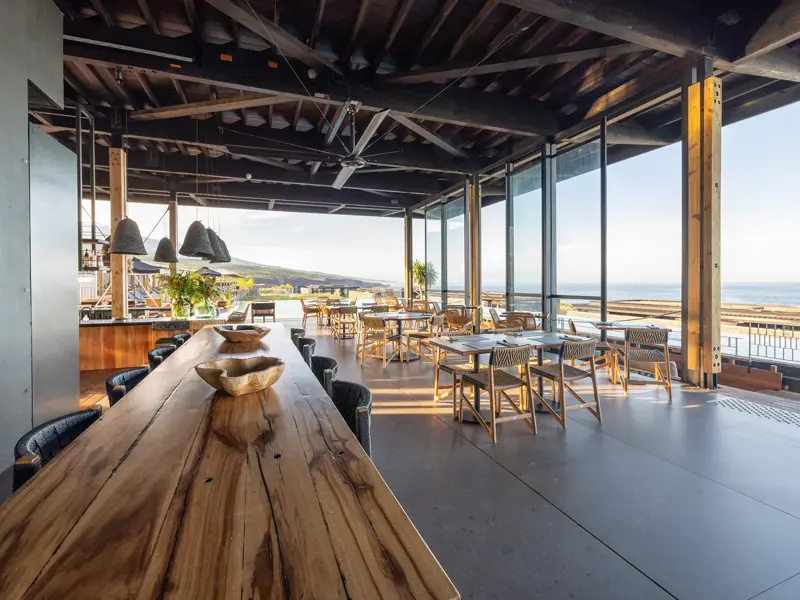 Das moderne Restaurant im Wood Hotel & Spa auf La Réunion mit langem Holztisch und Panoramablick auf das Meer im Abendlicht.
