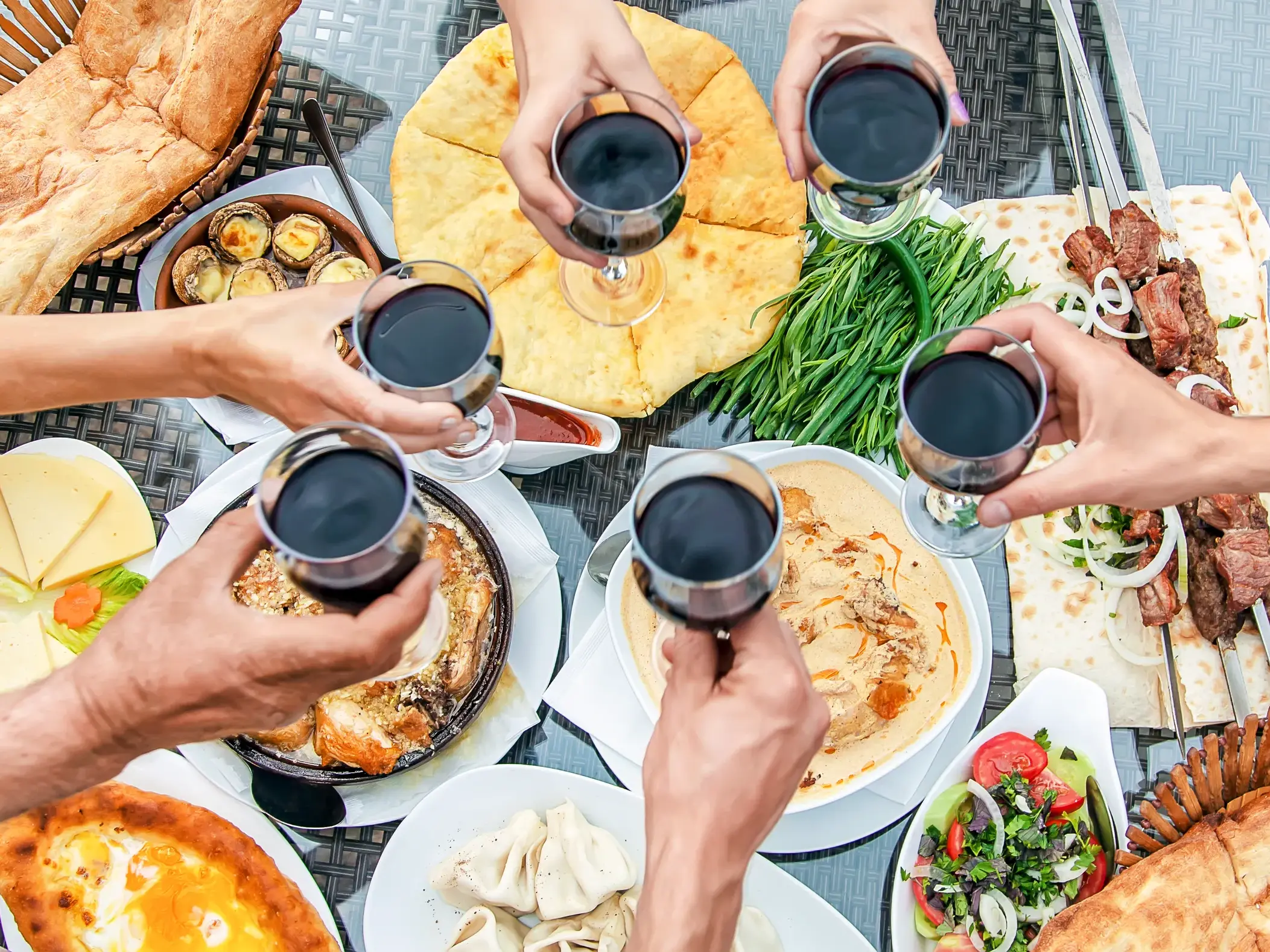 Eine Reisegruppe stößt mit Rotwein über einem reich gedeckten Tisch mit georgischen Spezialitäten wie Khinkali und Schaschlik an.