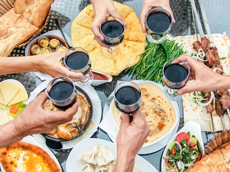 Eine Reisegruppe stößt mit Rotwein über einem reich gedeckten Tisch mit georgischen Spezialitäten wie Khinkali und Schaschlik an.