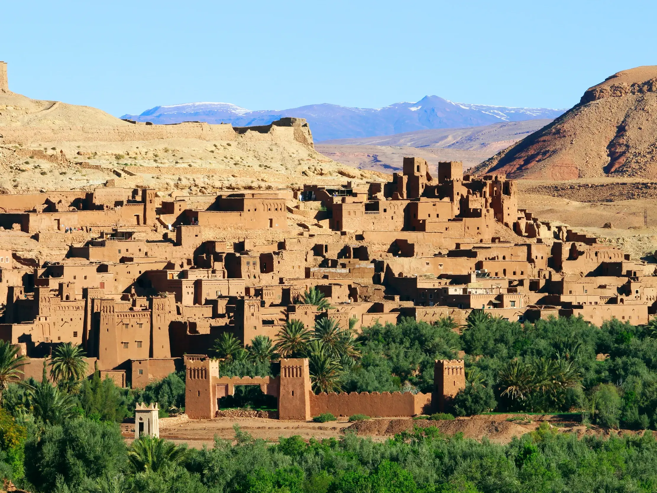 Die Lehmbausiedlung Ait Benhaddou in Marokko, eingebettet in eine grüne Oase vor dem schneebedeckten Hohen Atlas.