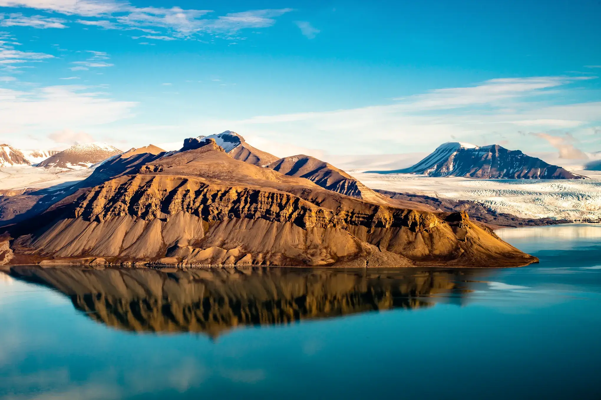 Die karge Berglandschaft von SPITZBERGEN spiegelt sich im türkisen Wasser des BILLEFJORD vor weiten Gletschern unter blauem Himmel.