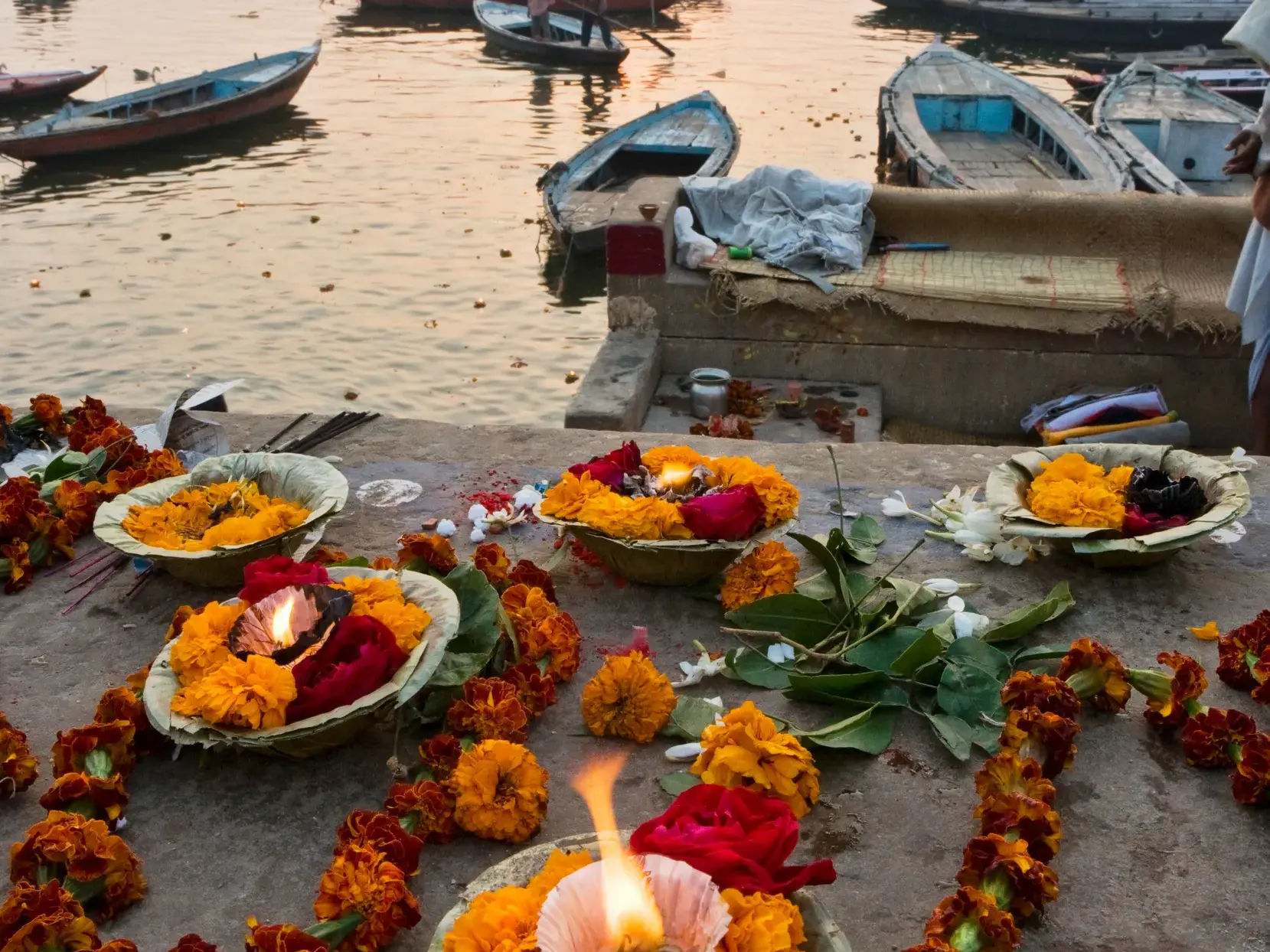 Opferschälchen mit brennenden Kerzen und Blumen an den Steinstufen des Ganges in Varanasi während einer spirituellen Zeremonie.