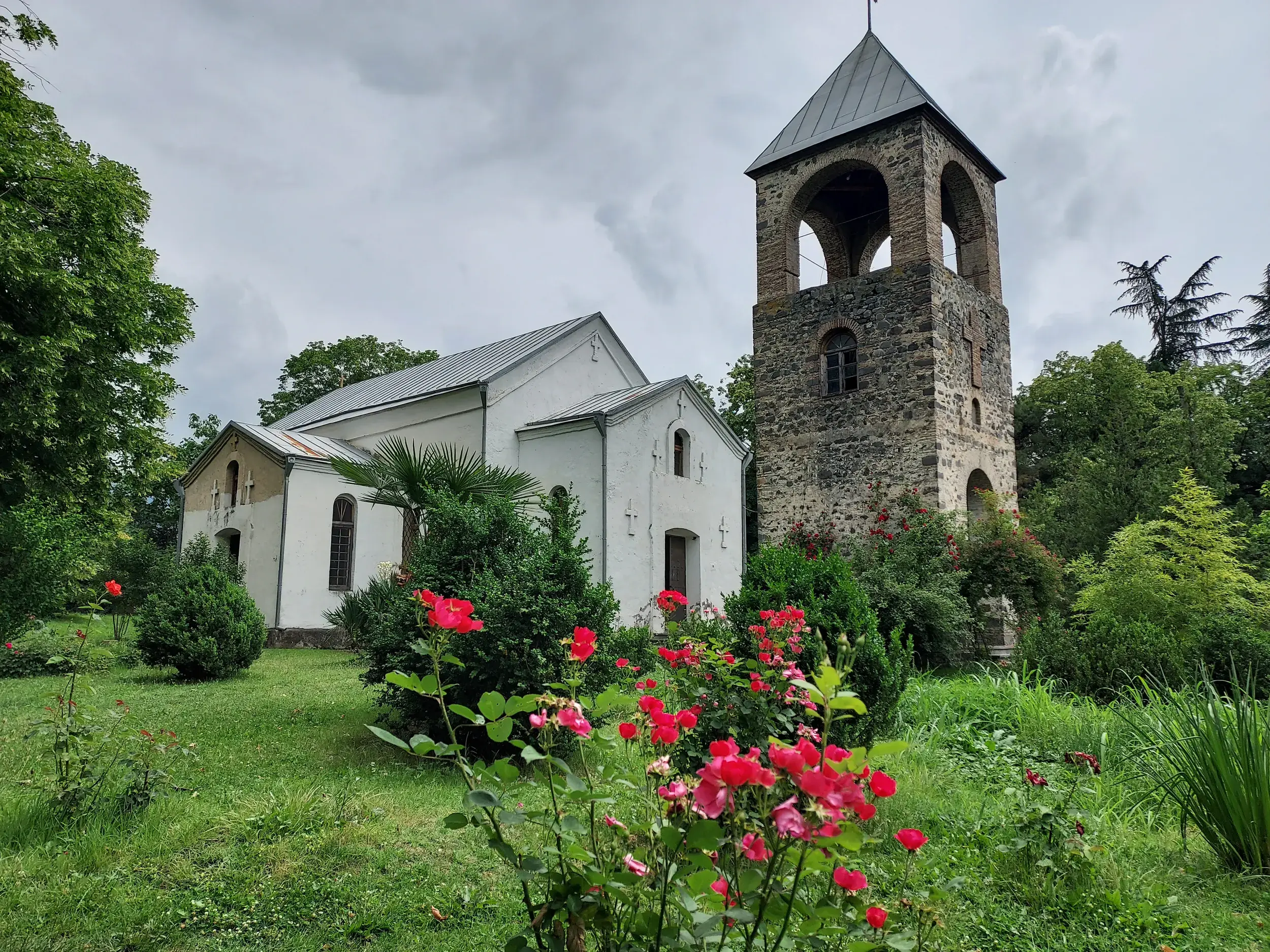 Die alte albanische Kirche von Kish bei Sheki in Aserbaidschan mit Steinturm, umgeben von einem grünen, blühenden Garten.