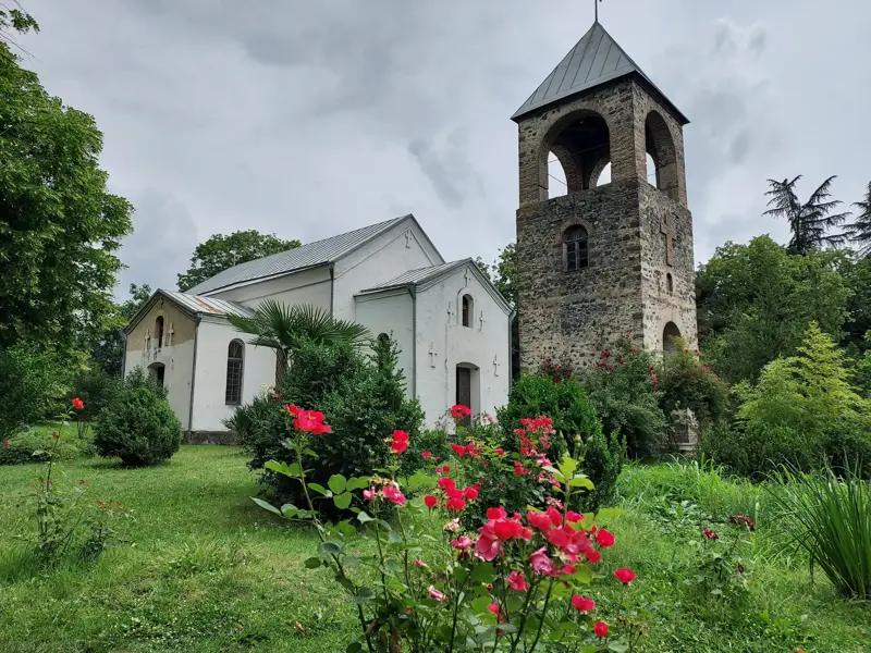 Die alte albanische Kirche von Kish bei Sheki in Aserbaidschan mit Steinturm, umgeben von einem grünen, blühenden Garten.