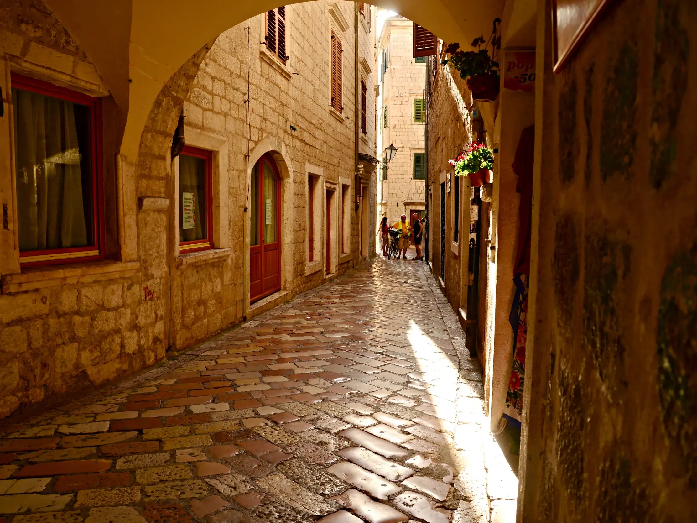 Verwinkelte Gasse mit Kopfsteinpflaster in der Altstadt von Kotor, Montenegro, beleuchtet von warmem Sonnenlicht auf den Steinfassaden.