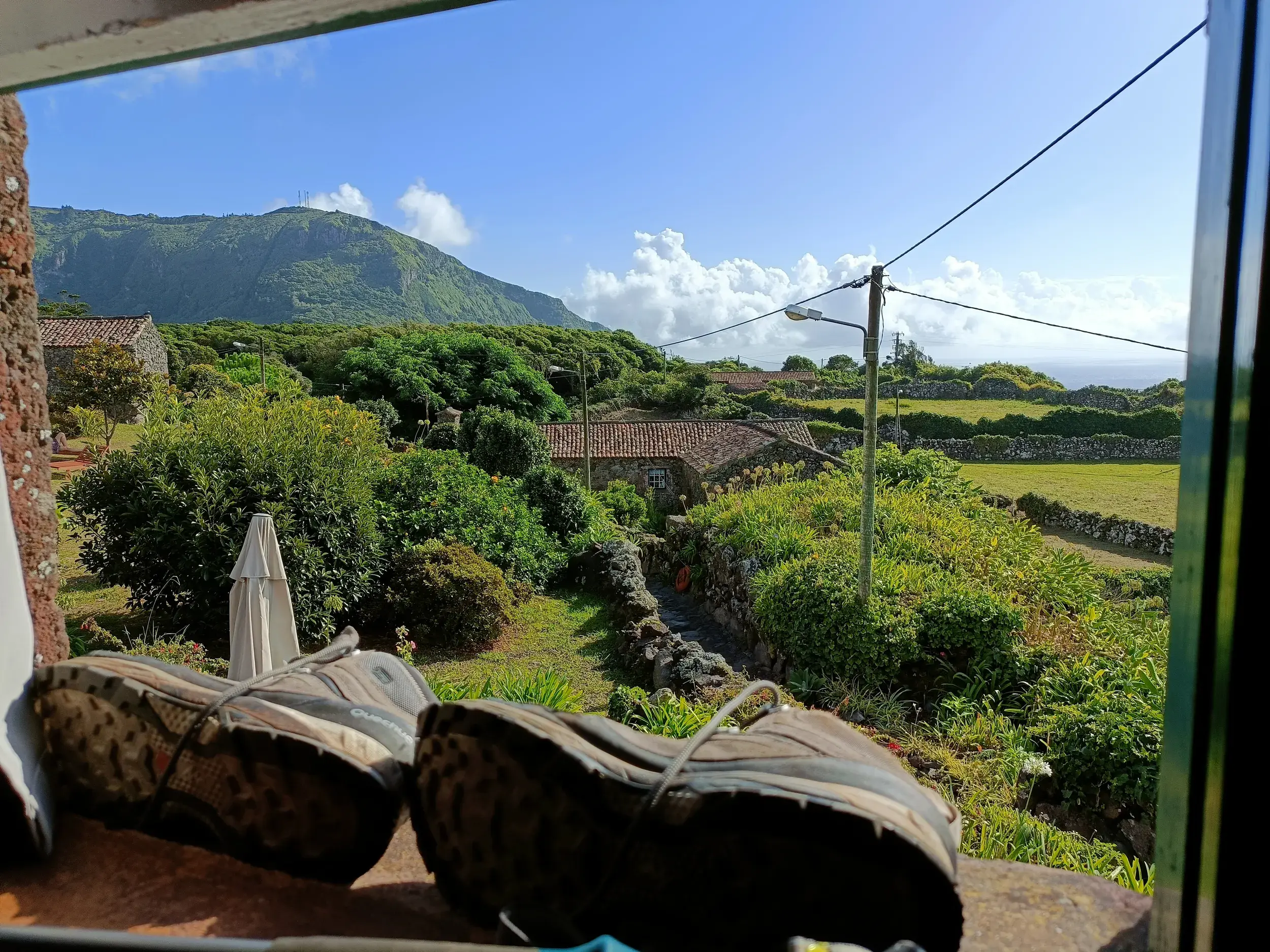 Wanderschuhe auf der Fensterbank der Unterkunft Aldeia da Cuada mit Blick auf die grüne Vulkanlandschaft der Insel Flores.