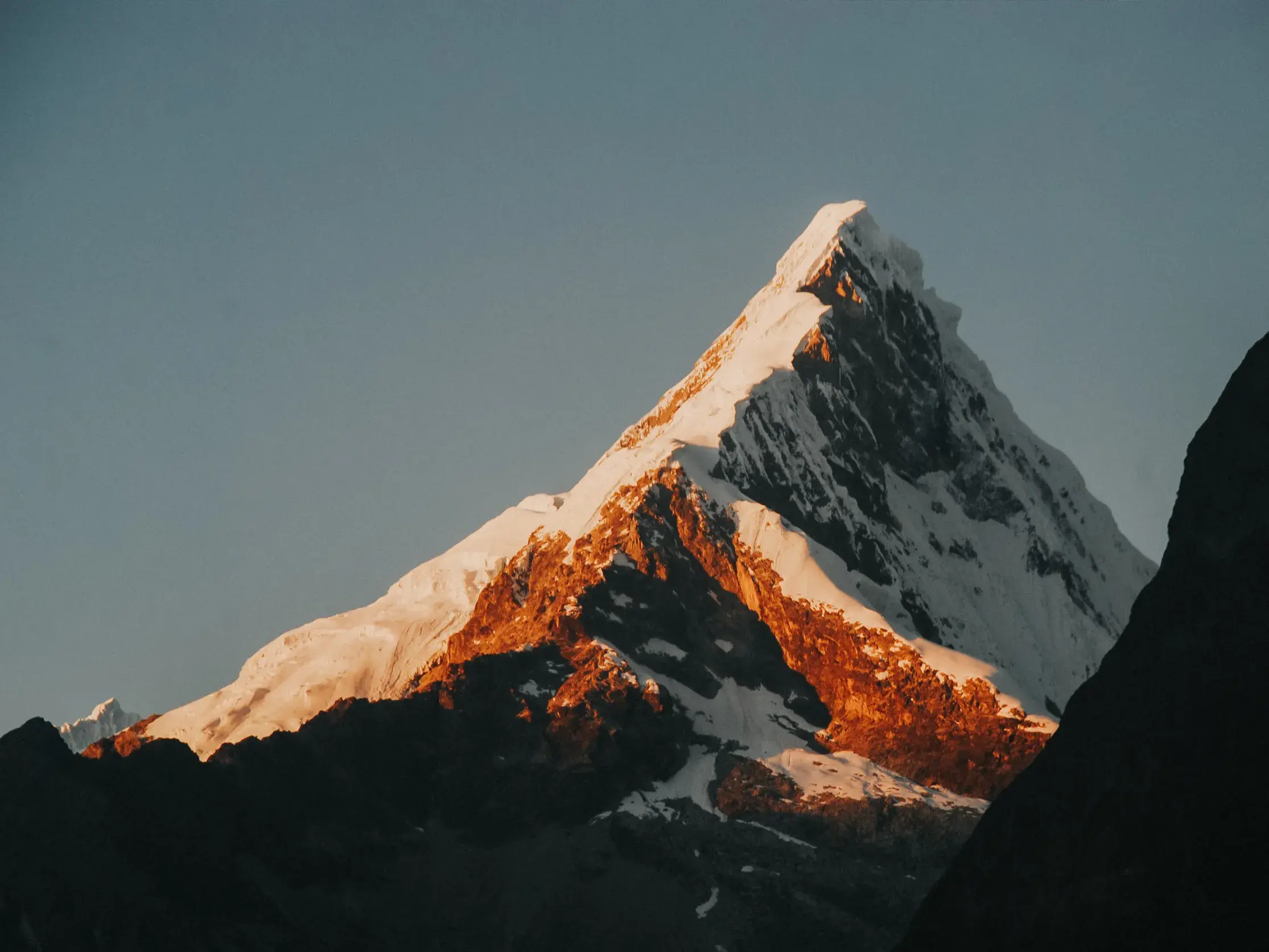 Der schneebedeckte Gipfel des Alpamayo in der Cordillera Blanca wird von der Abendsonne in goldenes Licht getaucht.