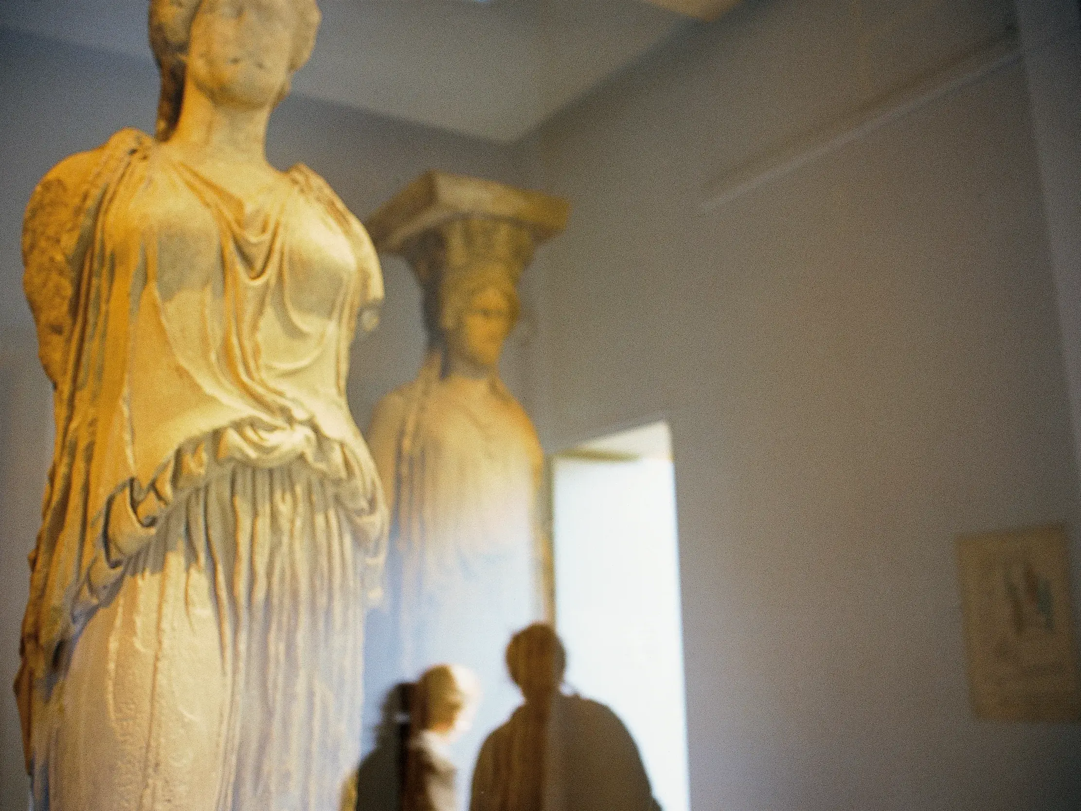 Detailreiche, antike Marmorstatue einer Frau im Akropolismuseum in Athen, die von Besuchern betrachtet wird.