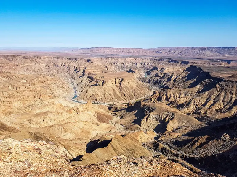 Weite Aussicht über die tiefen, sonnenbeschienenen Schluchten des Fish River Canyon in Namibia unter klarem Himmel.