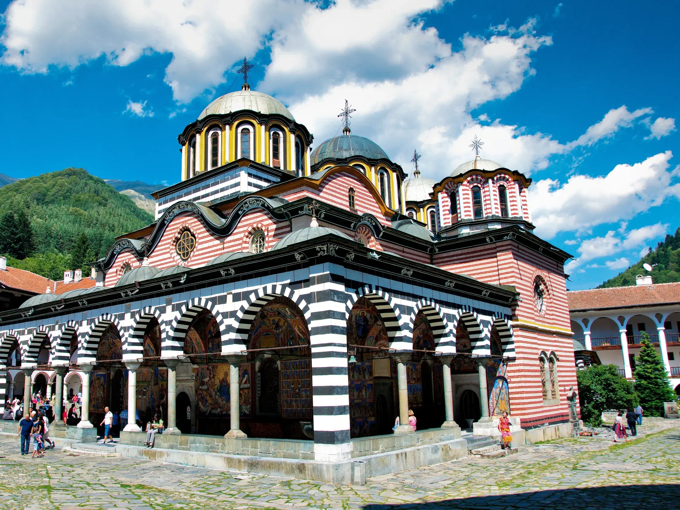 Das orthodoxe Rila-Kloster mit gestreiften Arkaden und bunten Fresken im Innenhof, umgeben vom Rila-Gebirge in Bulgarien.