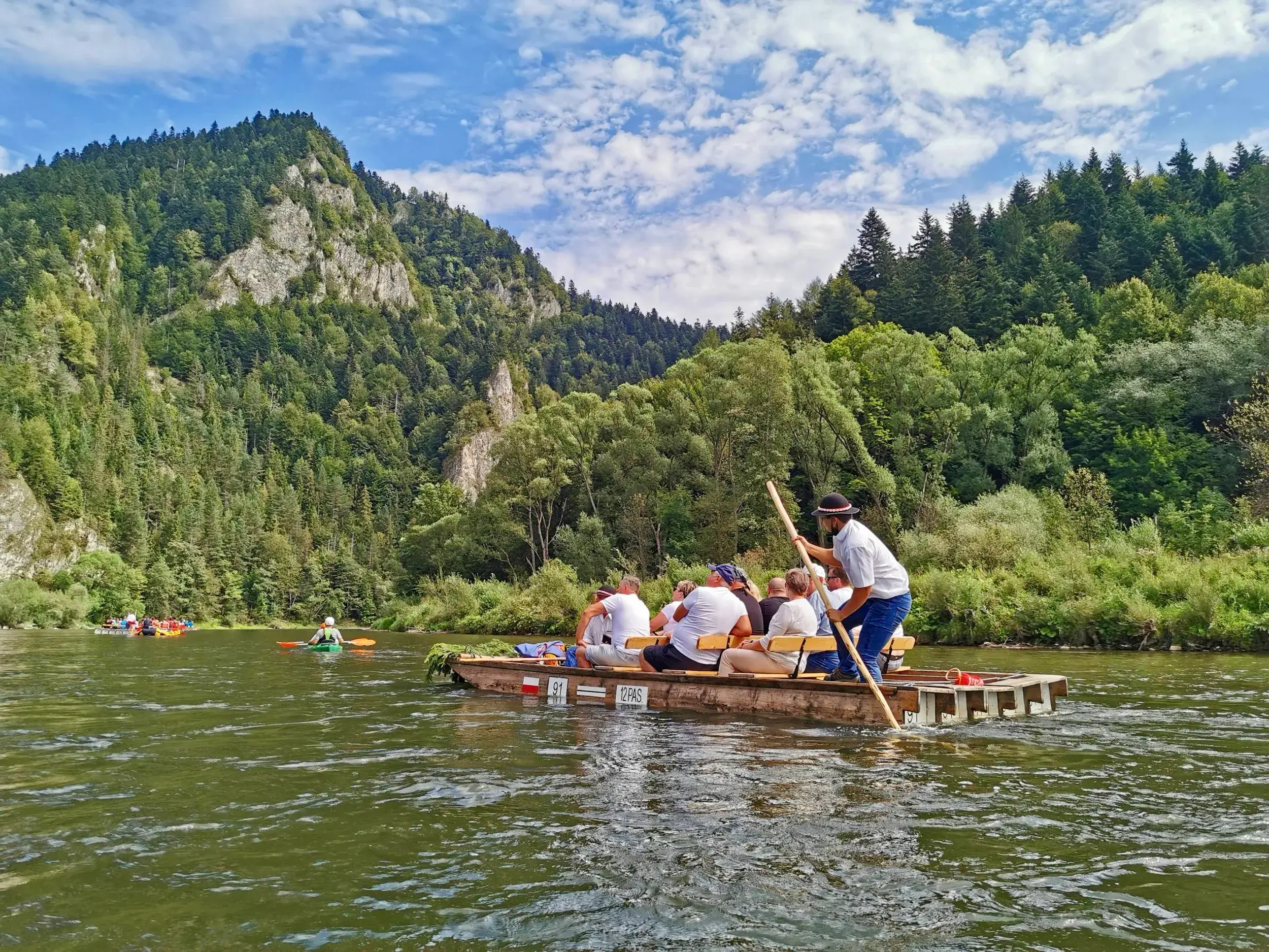 Reisegruppe auf einem traditionellen Holzfloß auf dem Fluss Dunajec, umgeben von der Felslandschaft des Pieniny-Nationalparks.