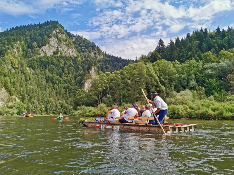 Reisegruppe auf einem traditionellen Holzfloß auf dem Fluss Dunajec, umgeben von der Felslandschaft des Pieniny-Nationalparks.