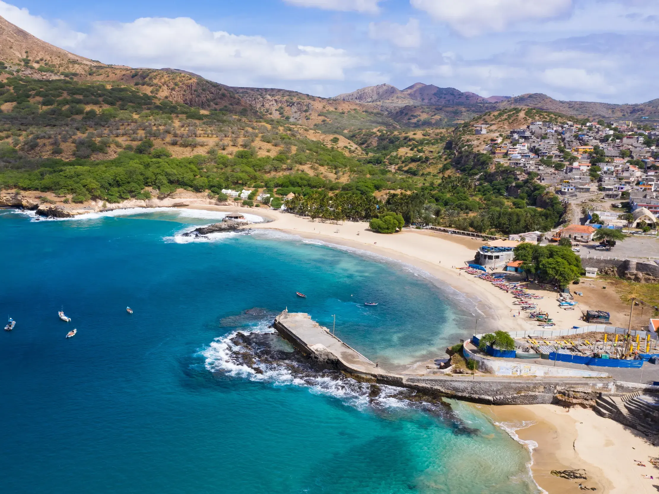 Malerische Bucht von Tarrafal auf Santiago mit türkisblauem Meer, Fischerbooten und dem Küstenort vor karger Berglandschaft.