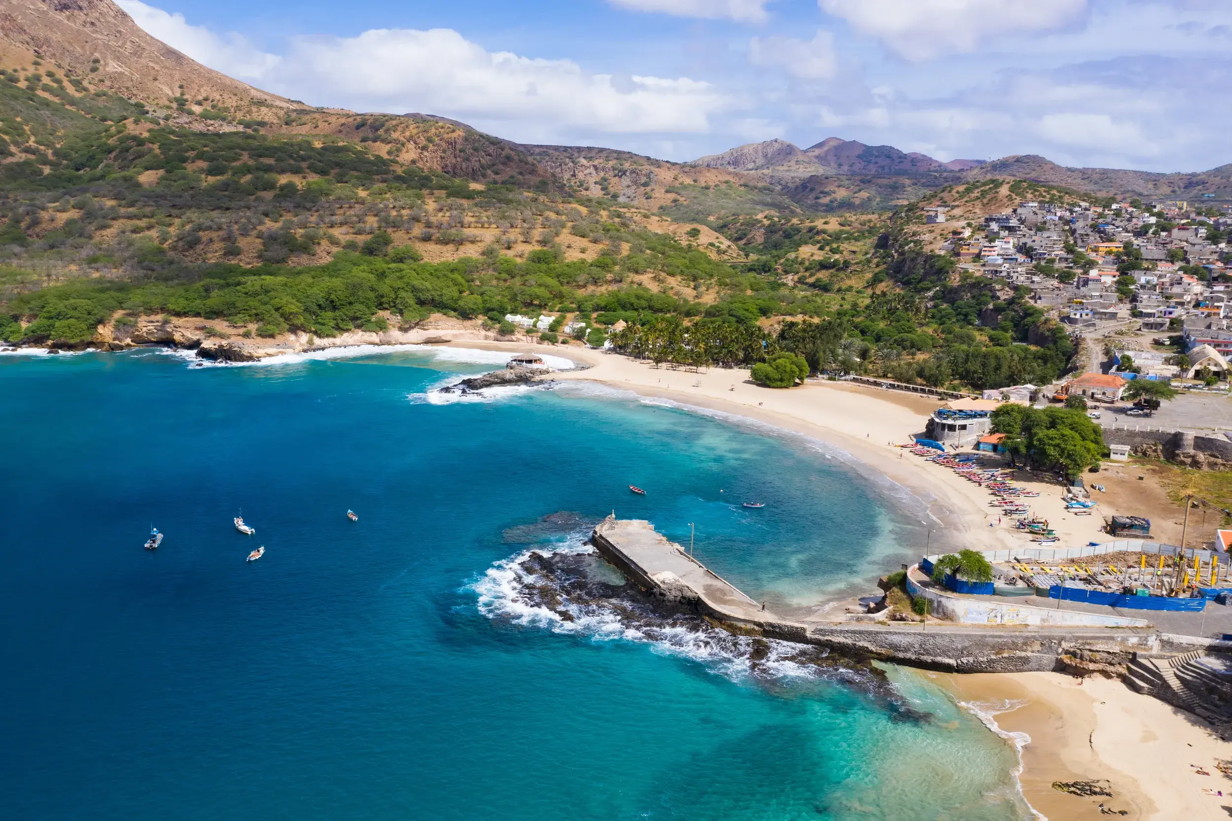 Malerische Bucht von Tarrafal auf Santiago mit türkisblauem Meer, Fischerbooten und dem Küstenort vor karger Berglandschaft.
