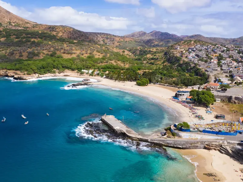 Luftaufnahme der Bucht von Tarrafal auf Santiago mit türkisfarbenem Meer, Fischerbooten am Strand und Bergen im Hintergrund.