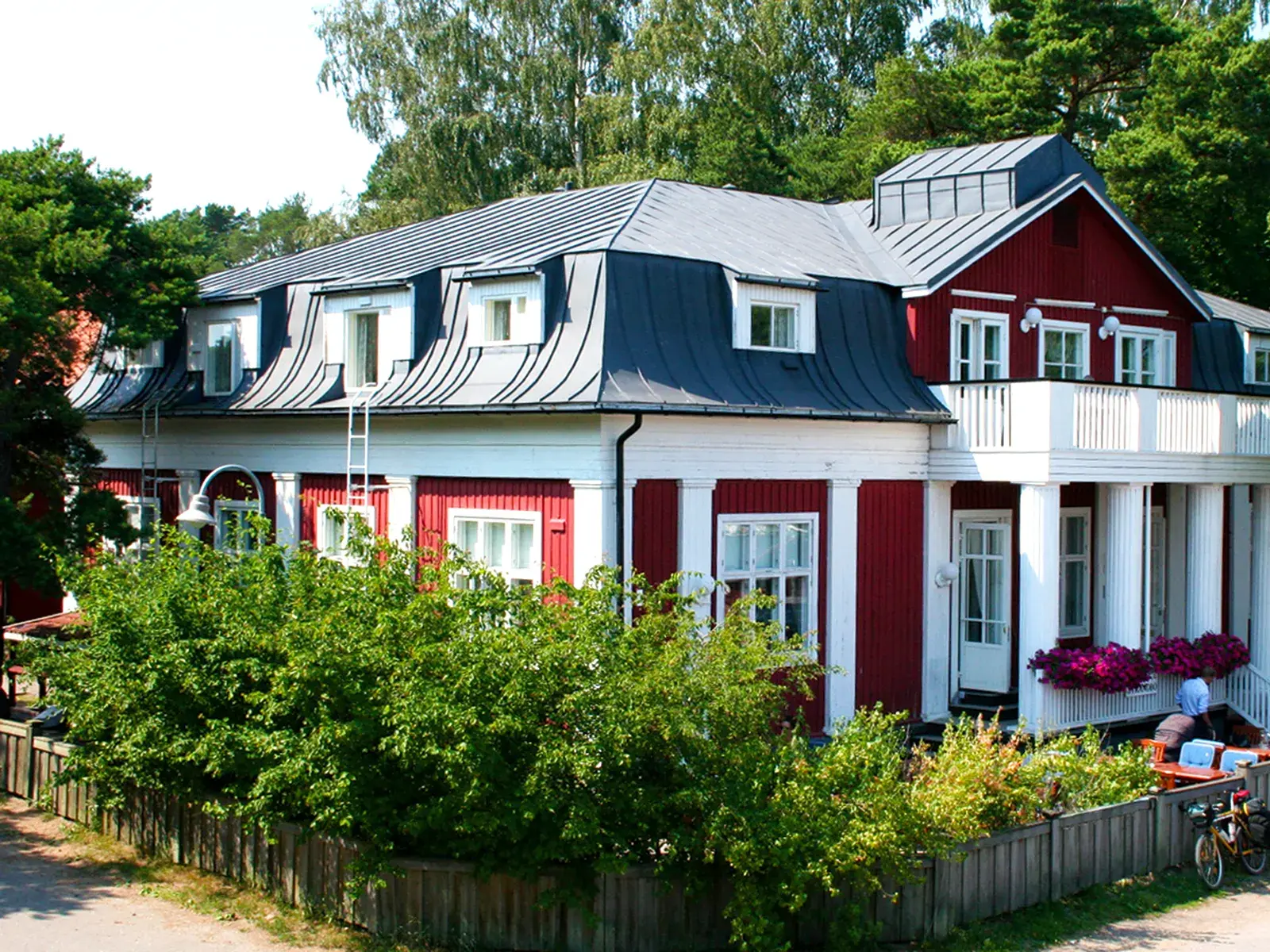 Das rote, hyggelige Holzhaus des Hotel Strandbo in Nagu, umgeben von Bäumen im finnischen Schärengarten.
