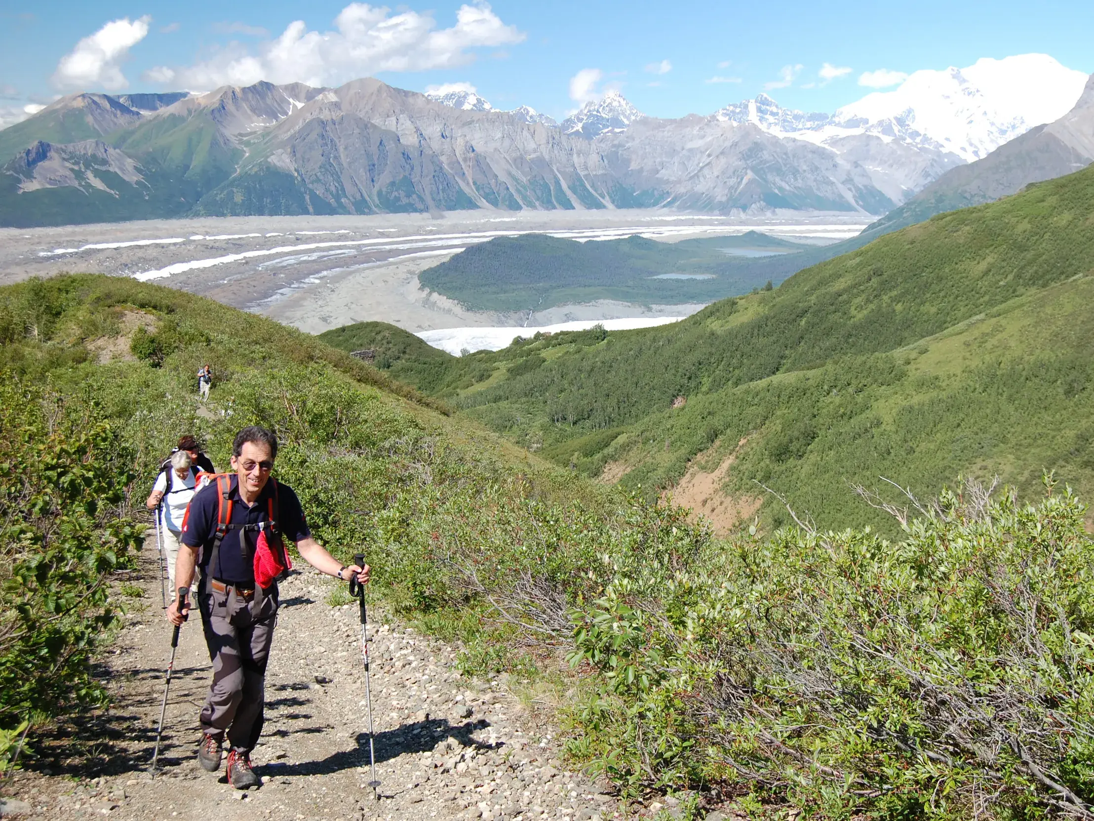 Wanderer auf einem schmalen Bergpfad im Kluane-Nationalpark mit Panoramablick auf ein weites Gletschertal und die St. Elias Mountains.