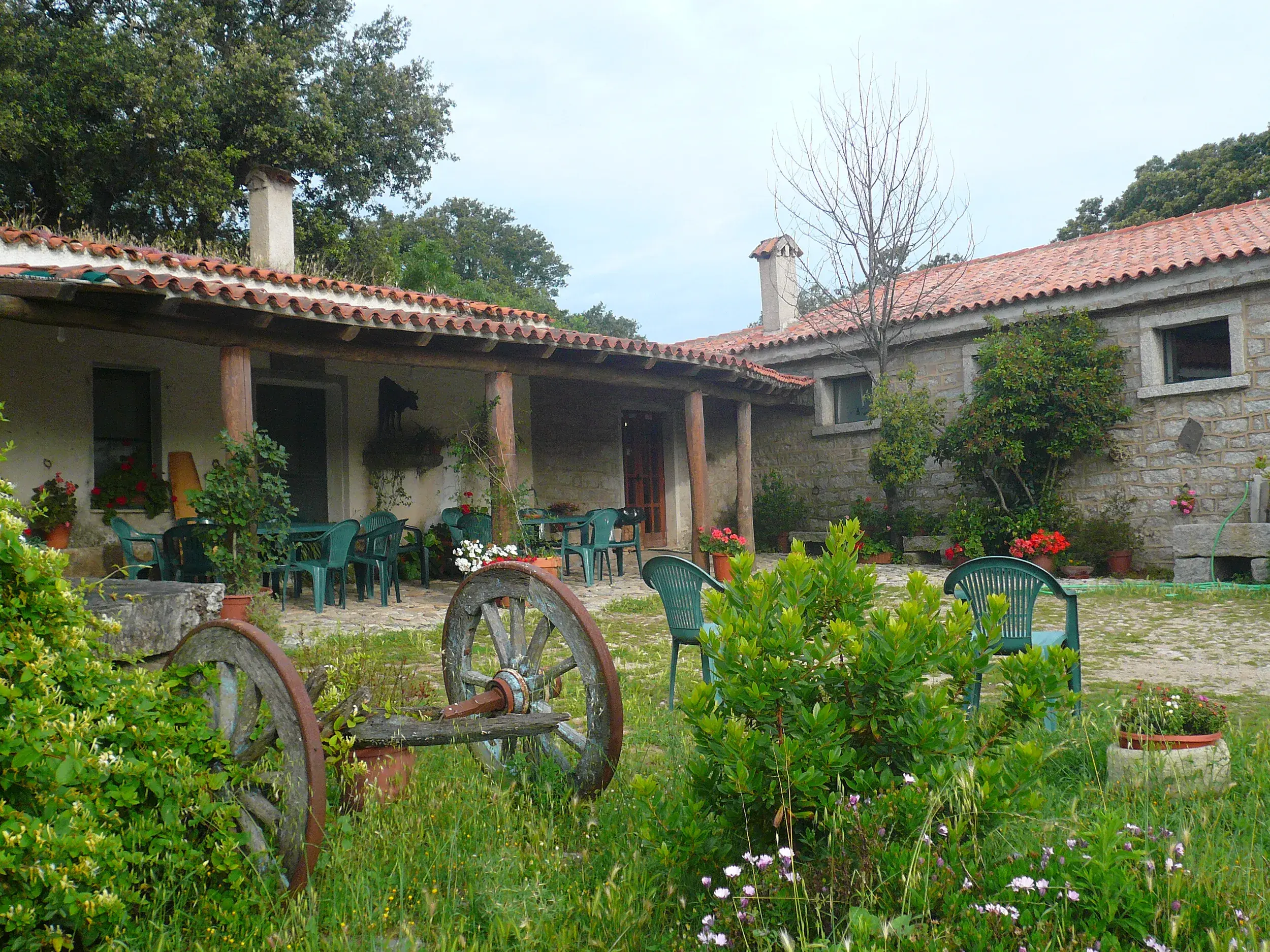 Idyllischer Innenhof eines traditionellen Bauernhofs auf Sardinien mit rustikalem Steingebäude und Sitzgelegenheiten.