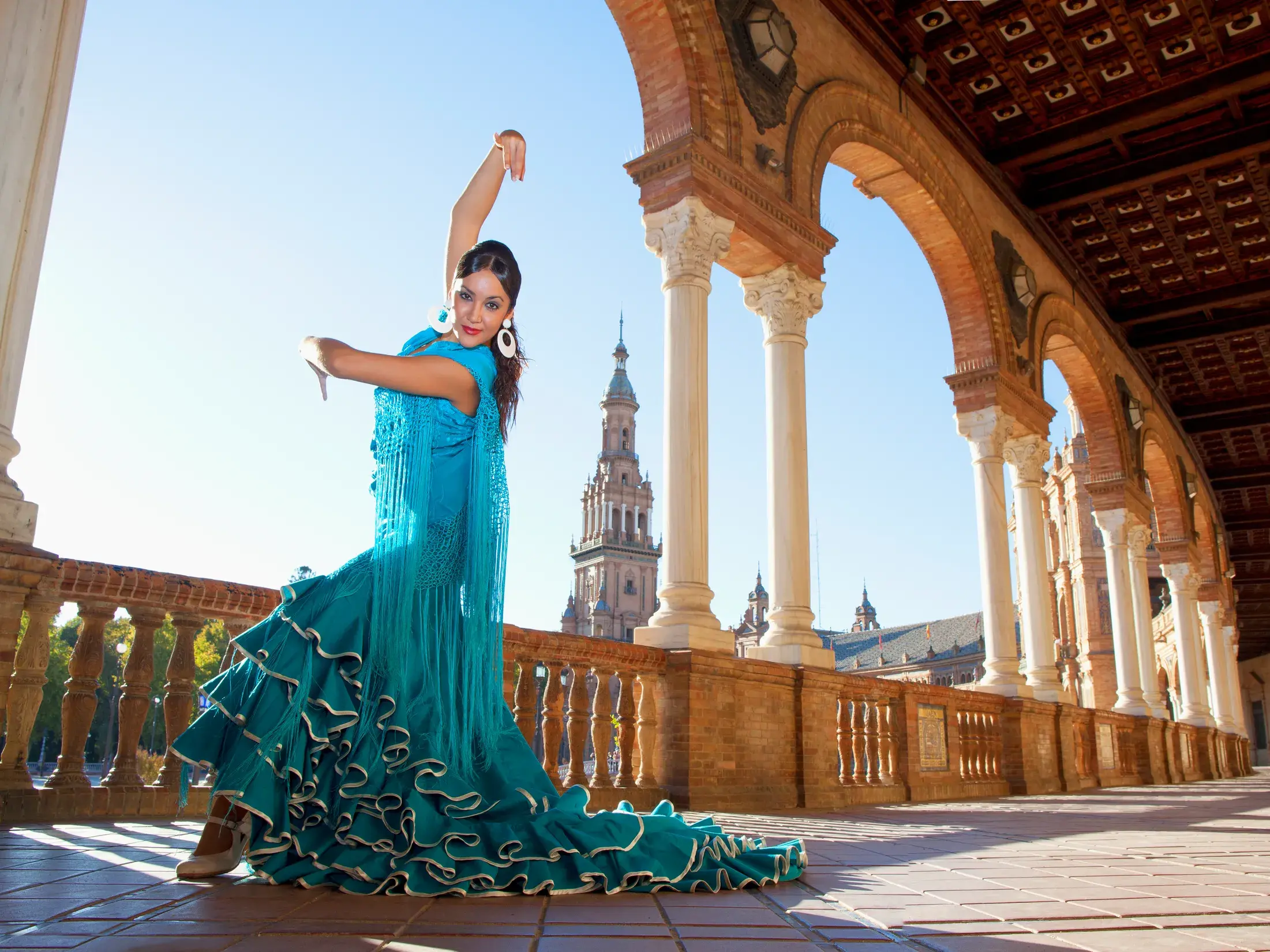 Eine Flamenco-Tänzerin in einem türkisen Kleid tanzt unter den sonnigen Arkaden der Plaza de España in Sevilla, Andalusien.