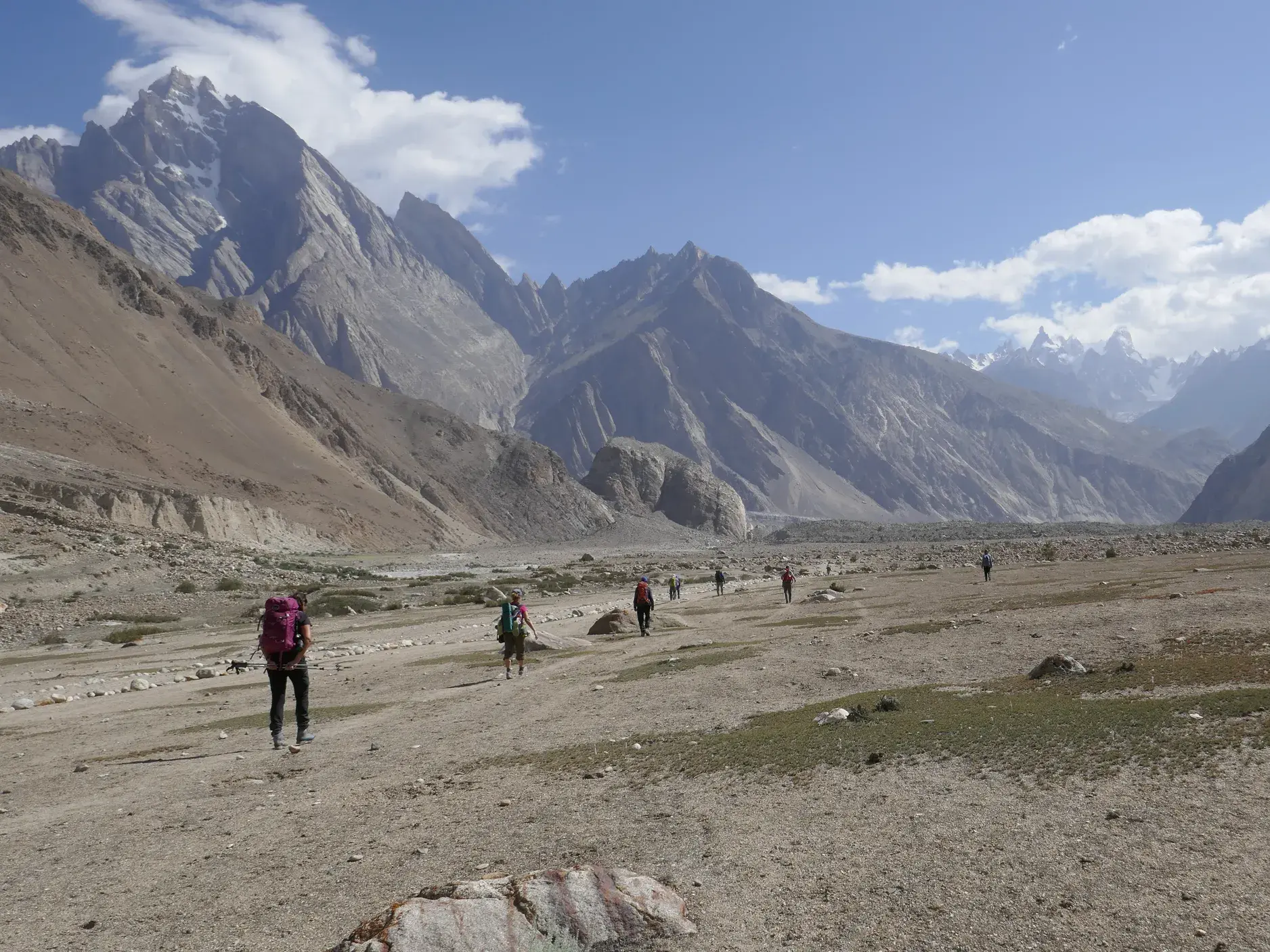 Hauser-Trekkinggruppe wandert über eine weite Gletschermoräne im Karakorum mit Blick auf schroffe Berggipfel in Pakistan.