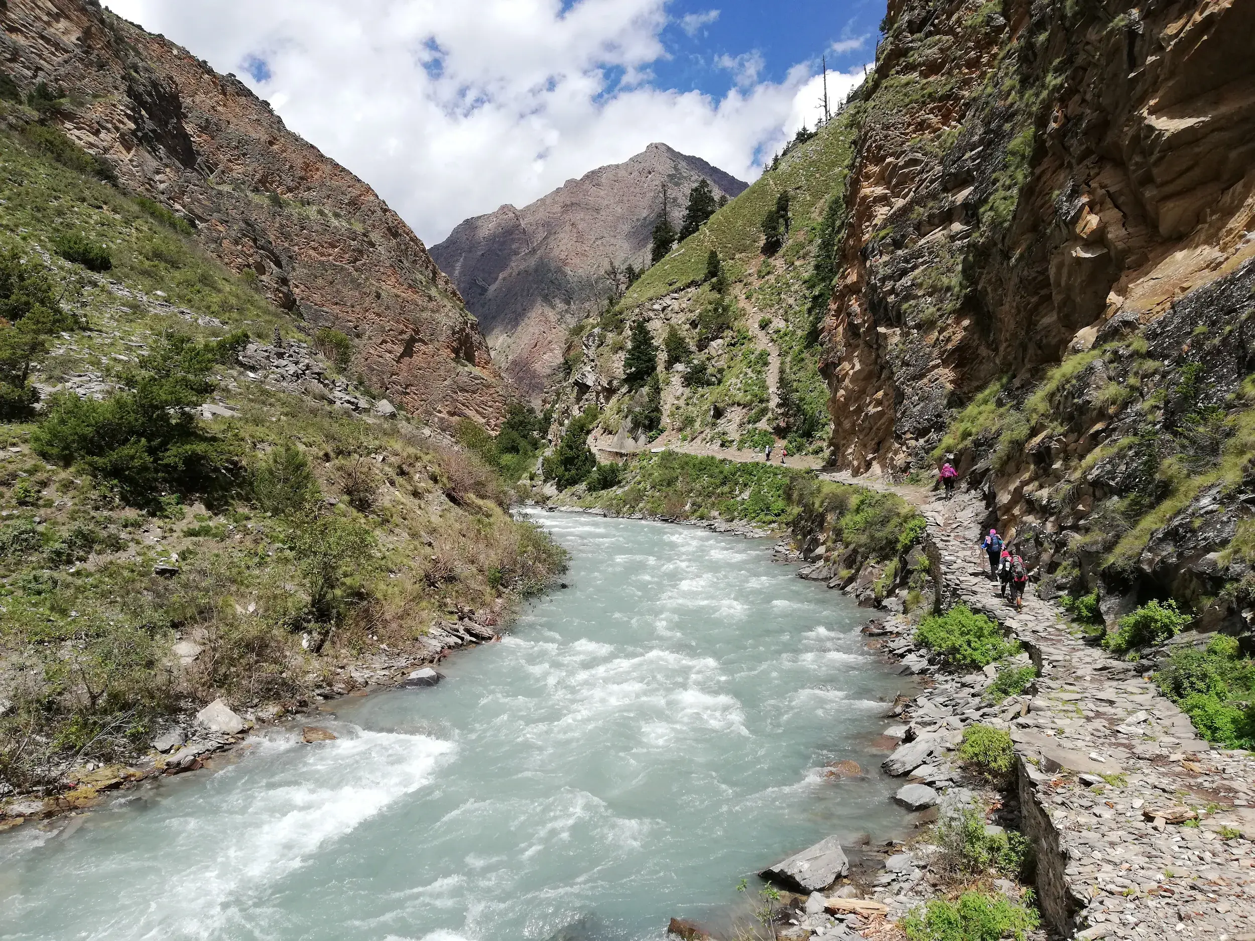 Eine Trekking-Gruppe wandert auf einem Steinpfad am reißenden Tarap Khola Fluss durch eine tiefe Schlucht in der Dolpo-Region, Nepal.