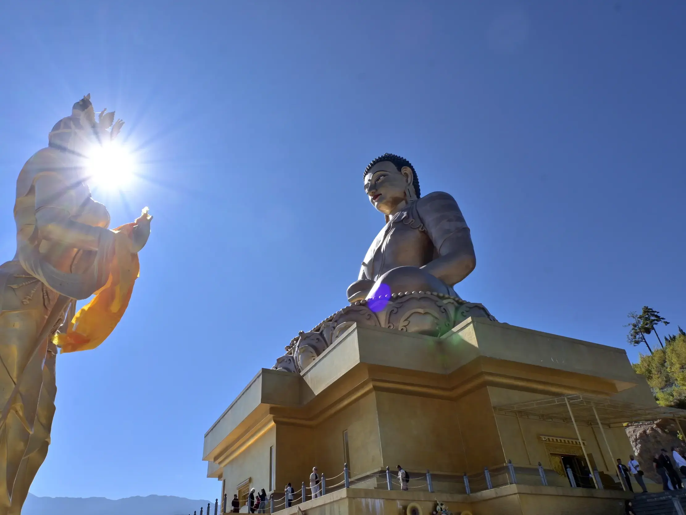Die monumentale Buddha Dordenma Statue in Thimphu neben einer goldenen Figur, die im hellen Gegenlicht der Sonne erstrahlt.