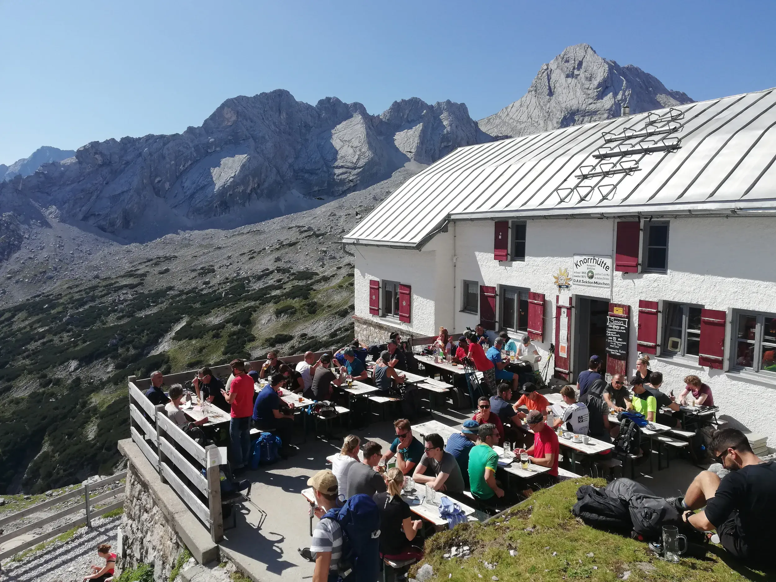 Wanderer bei einer Rast auf der Sonnenterrasse der Knorrhütte während der Alpenüberquerung durch das Wettersteingebirge.
