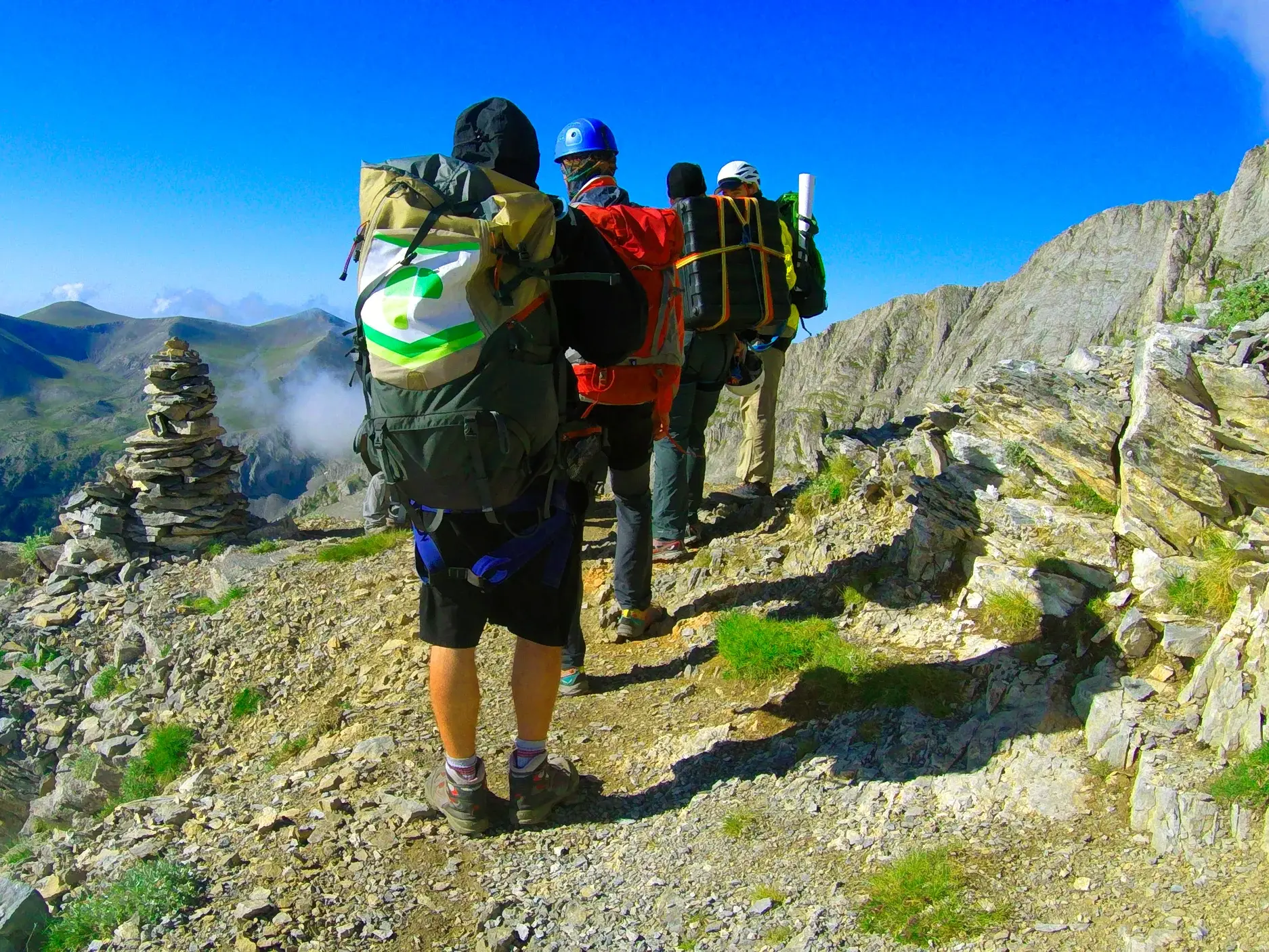 Eine Hauser-Reisegruppe beim Trekking auf einem schmalen Felsgrat im griechischen Olymp-Massiv unter strahlend blauem Himmel.
