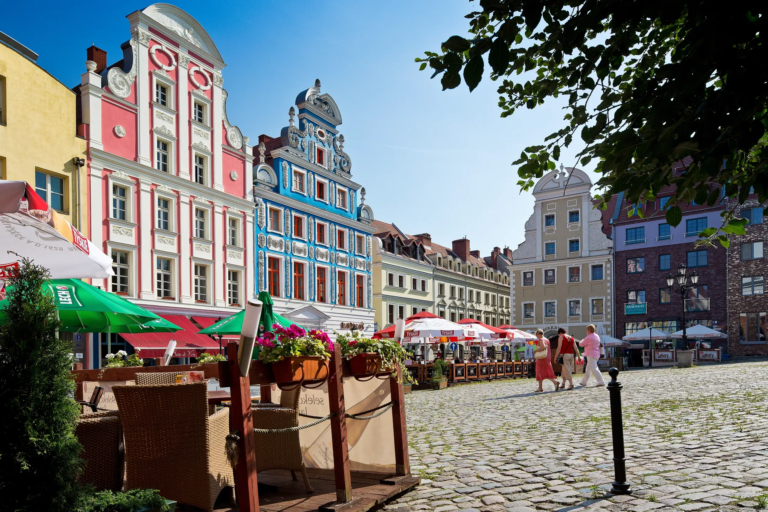 Bunte Giebelhäuser am historischen Marktplatz in Stettin (Szczecin) mit Außengastronomie an einem sonnigen Tag.