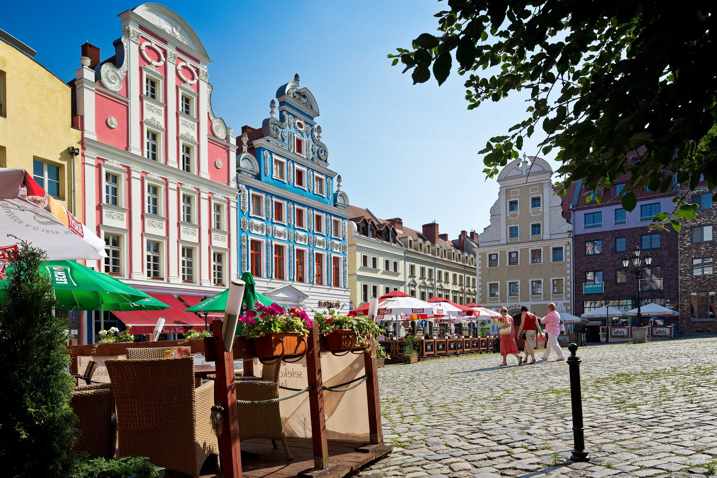 Bunte Giebelhäuser am historischen Marktplatz in Stettin (Szczecin) mit Außengastronomie an einem sonnigen Tag.