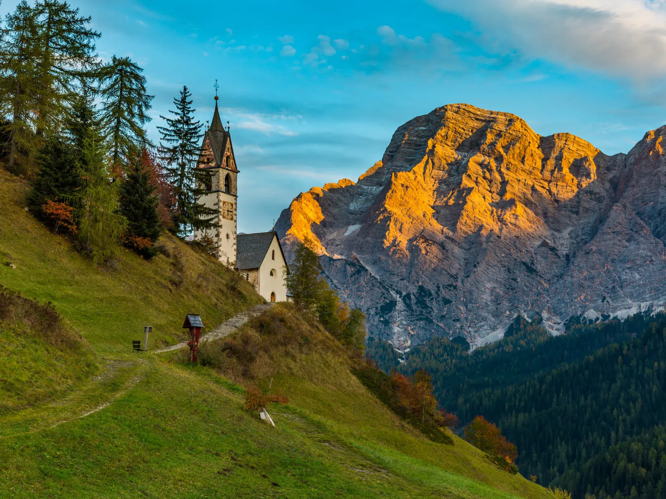 Idyllische Bergkirche auf einem Wanderweg in Südtirol mit Blick auf einen von der Morgensonne angestrahlten Dolomitengipfel.