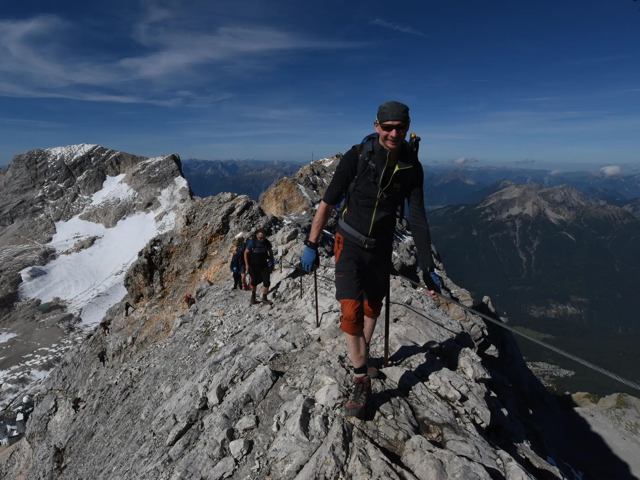 Wandergruppe auf dem finalen Aufstieg zur Zugspitze über den schmalen, mit Drahtseilen gesicherten Grat in den Alpen.