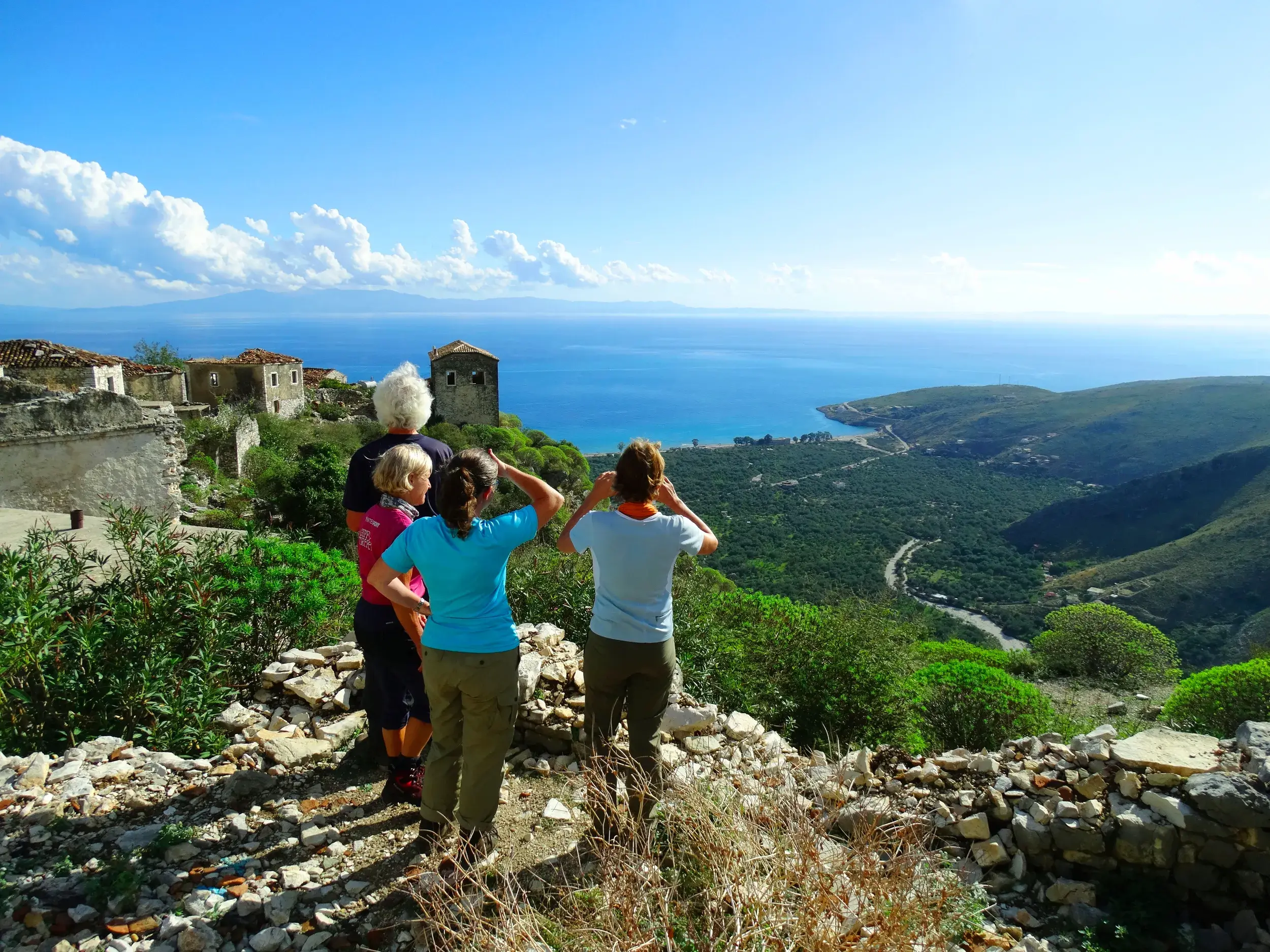 Kleine Wandergruppe blickt beim Trekking im Küstengebirge Albaniens von einem alten Bergdorf auf die Riviera.