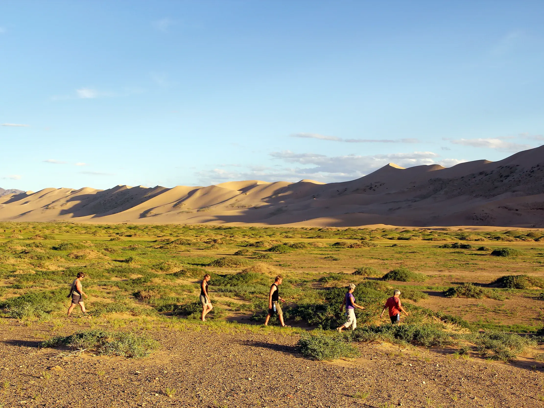 Kleine Wandergruppe auf einem Pfad durch die Steppe mit Blick auf die beeindruckenden Sanddünen von Khongoryn Els in der Mongolei.