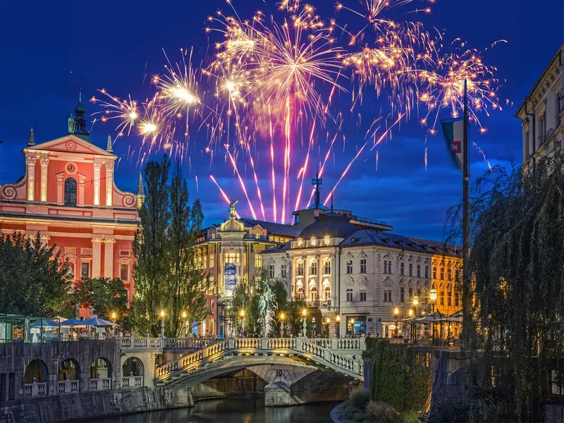 Festliches Silvesterfeuerwerk über den erleuchteten Drei Brücken und der malerischen Altstadt von Ljubljana bei Nacht.
