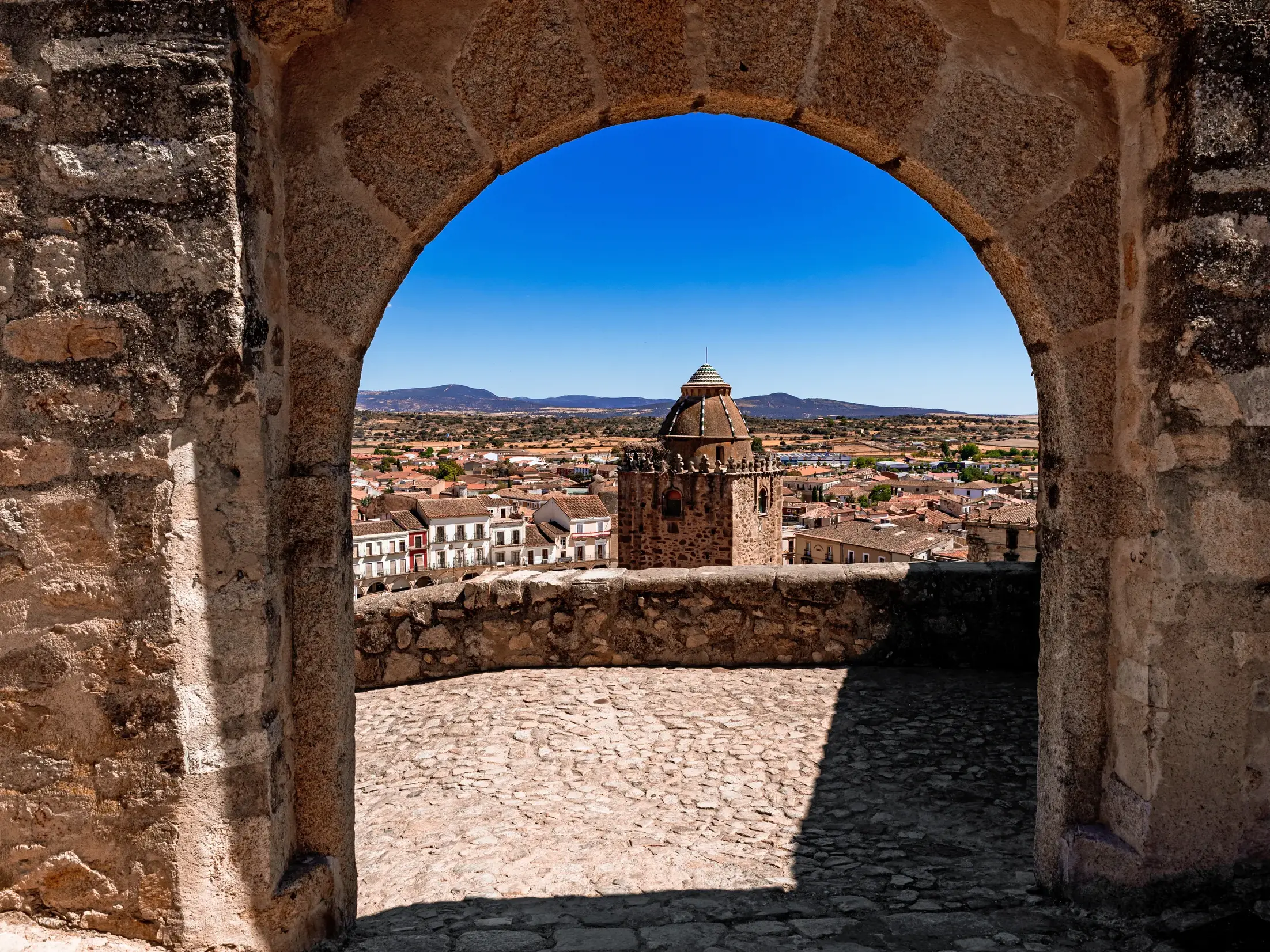 Sonniger Ausblick von der Stadtmauer durch einen Steinbogen auf die Altstadt von Trujillo in der Extremadura.
