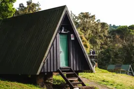 Rustikale Berghütte mit grüner Tür im Camp der Marangu-Route am Kilimanjaro, umgeben von üppiger Vegetation.