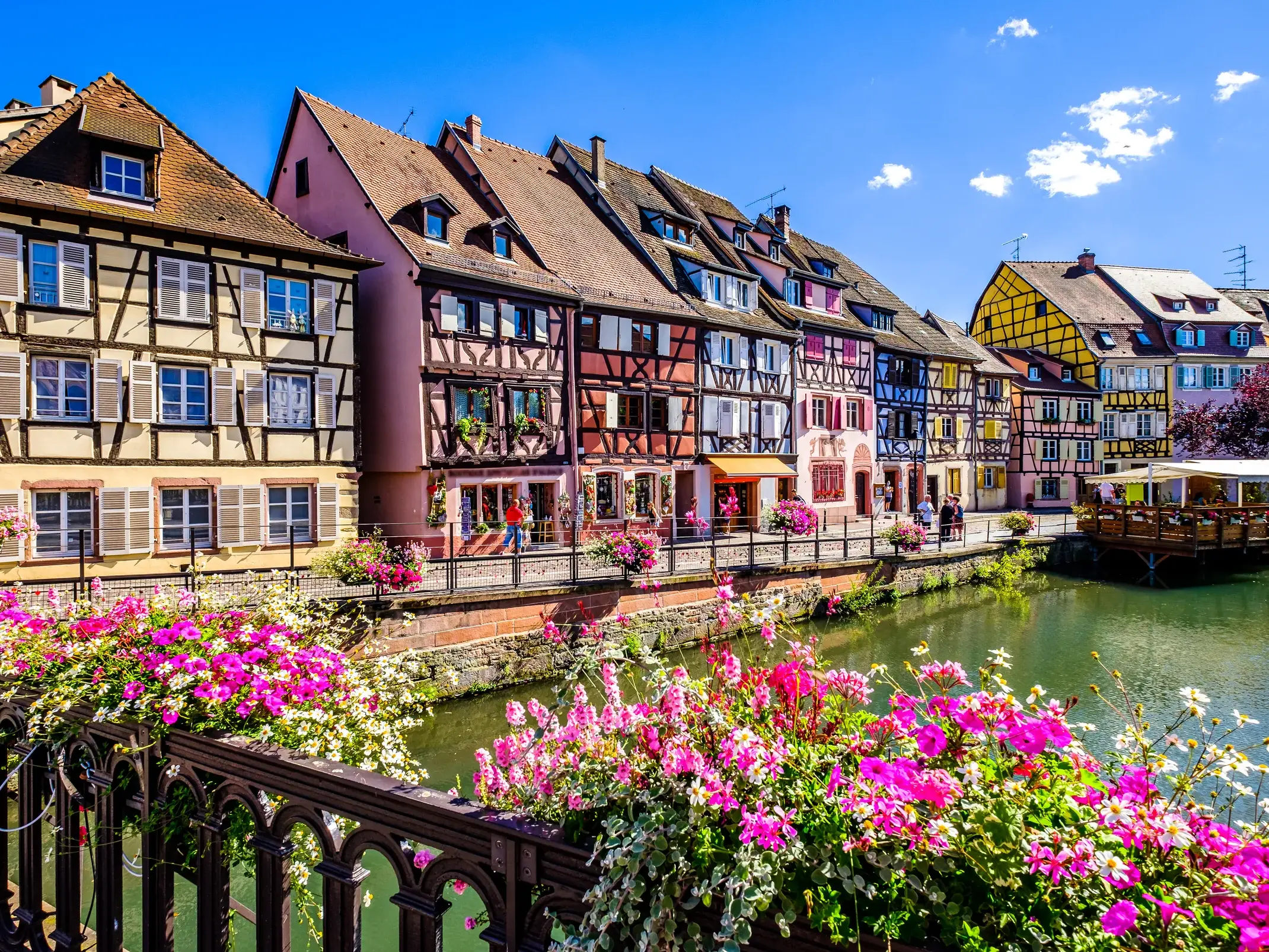 Blick von einer blumengeschmückten Brücke auf die farbenfrohen Fachwerkhäuser am Kanal in Colmar im Elsass.