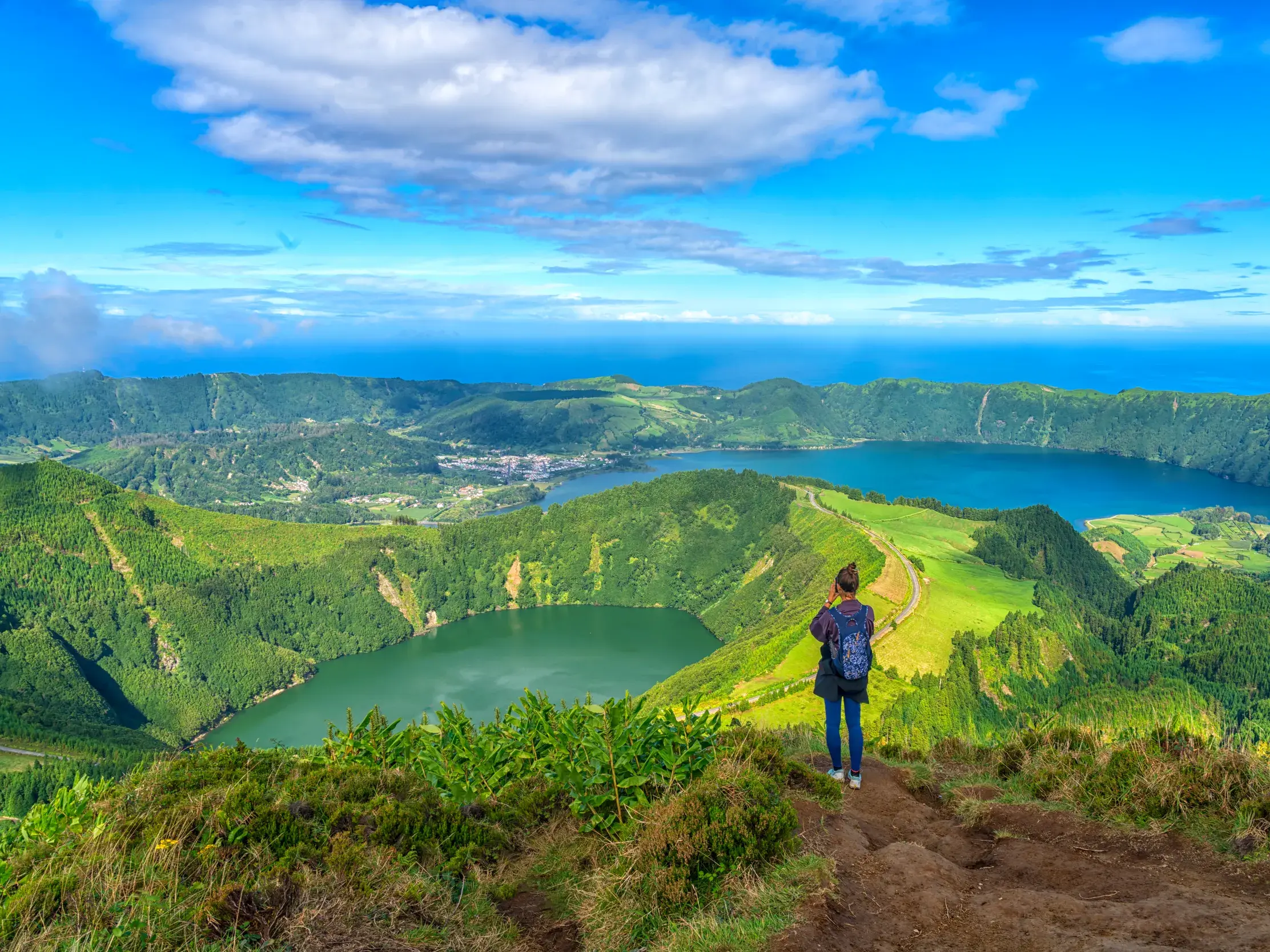 Eine Wanderin am Vista do Rei genießt den Ausblick auf die Vulkanseen Lagoa Azul und Lagoa Verde in der Caldeira von Sete Cidades.